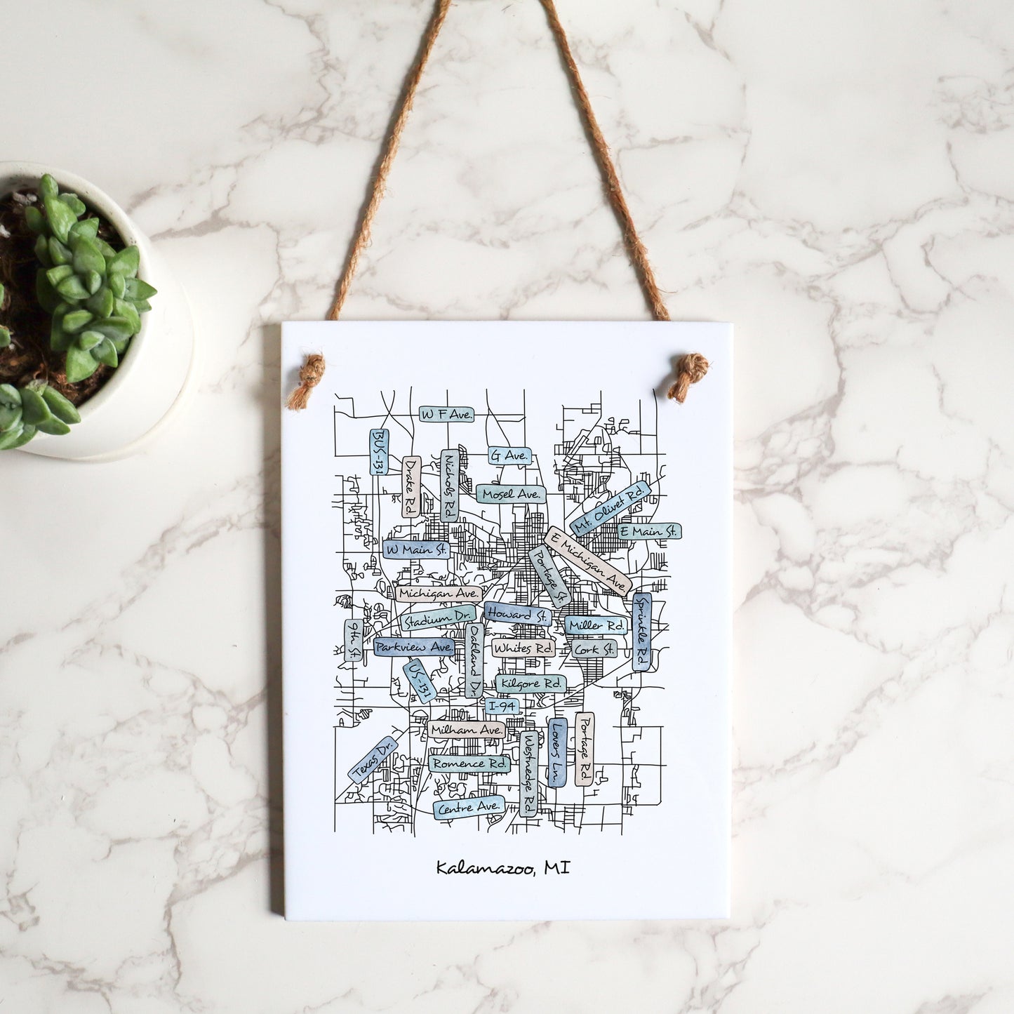 A custom city street map on a rectangle tile sign, hanging on a wall from hemp string