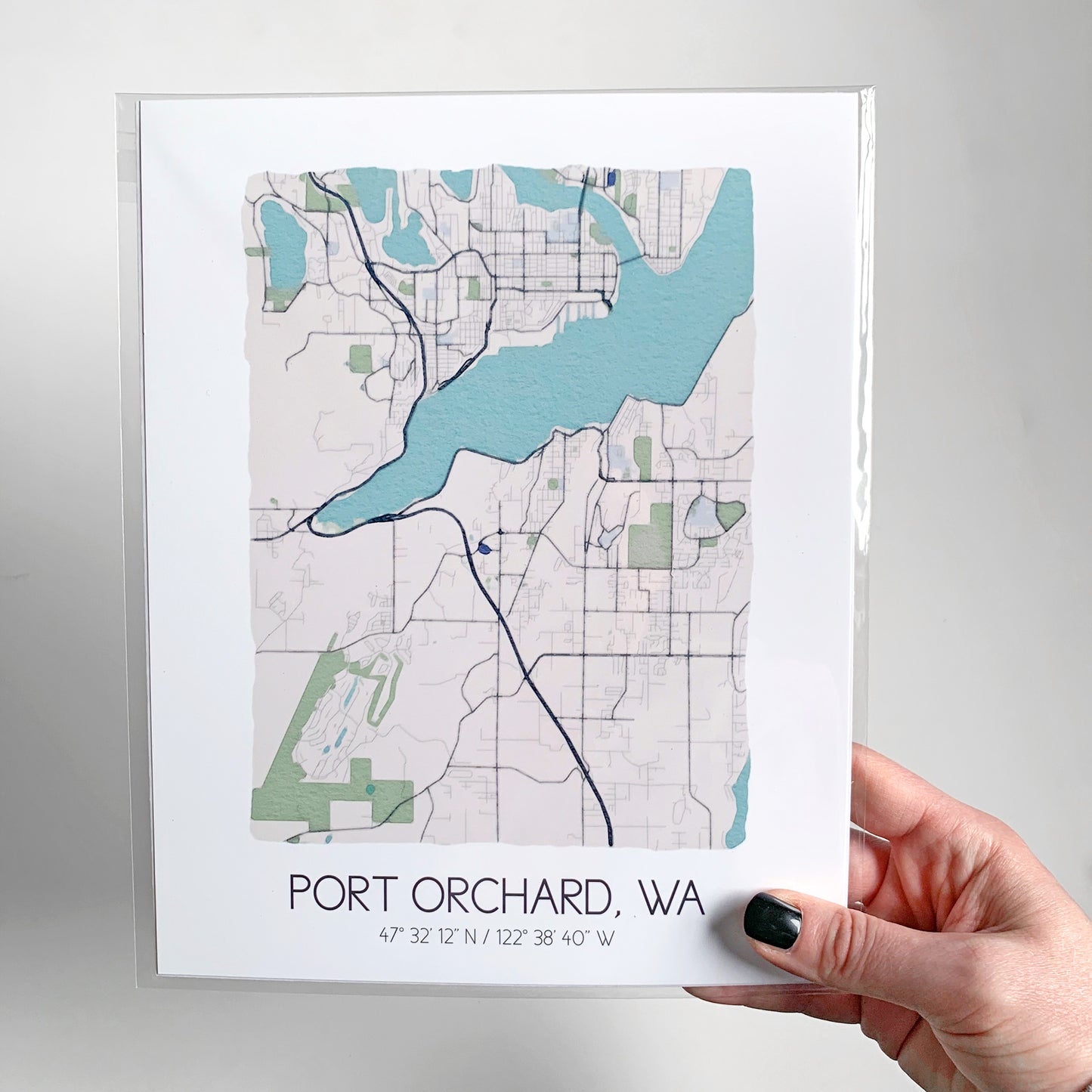 A hand holding a watercolor city map print packaged in a clear sleeve.
