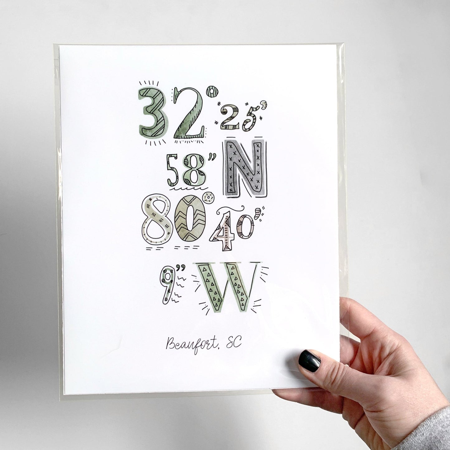 A hand holding a city coordinates print, packaged inside a clear sleeve.