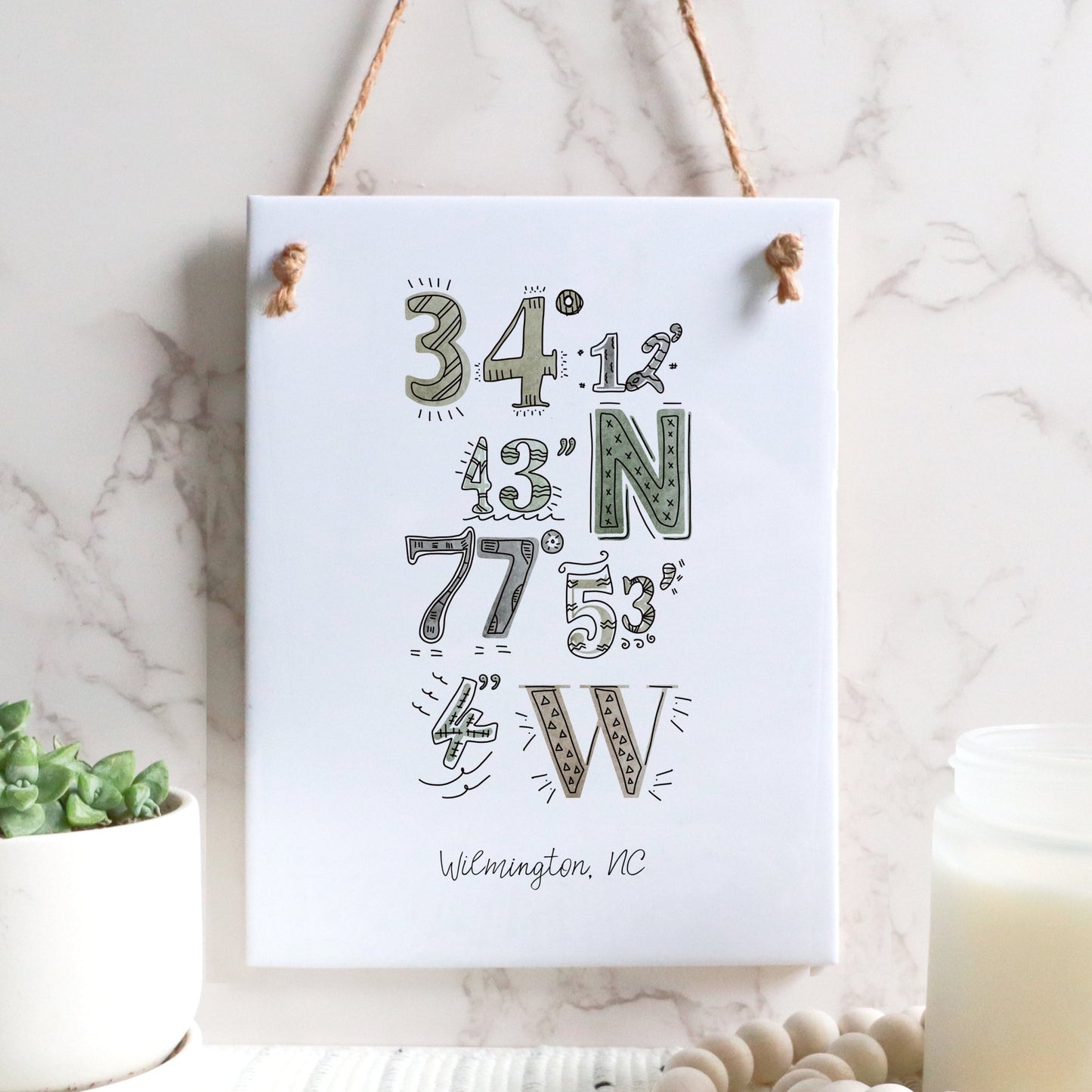 A city drawing of the coordinates of Wilmington NC on a rectangle tile sign, hanging on a wall, in the color earthy