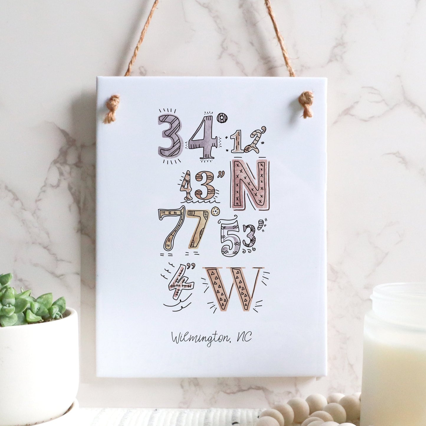 A city drawing of the coordinates of Wilmington NC on a rectangle tile sign, hanging on a wall, in the color sunset
