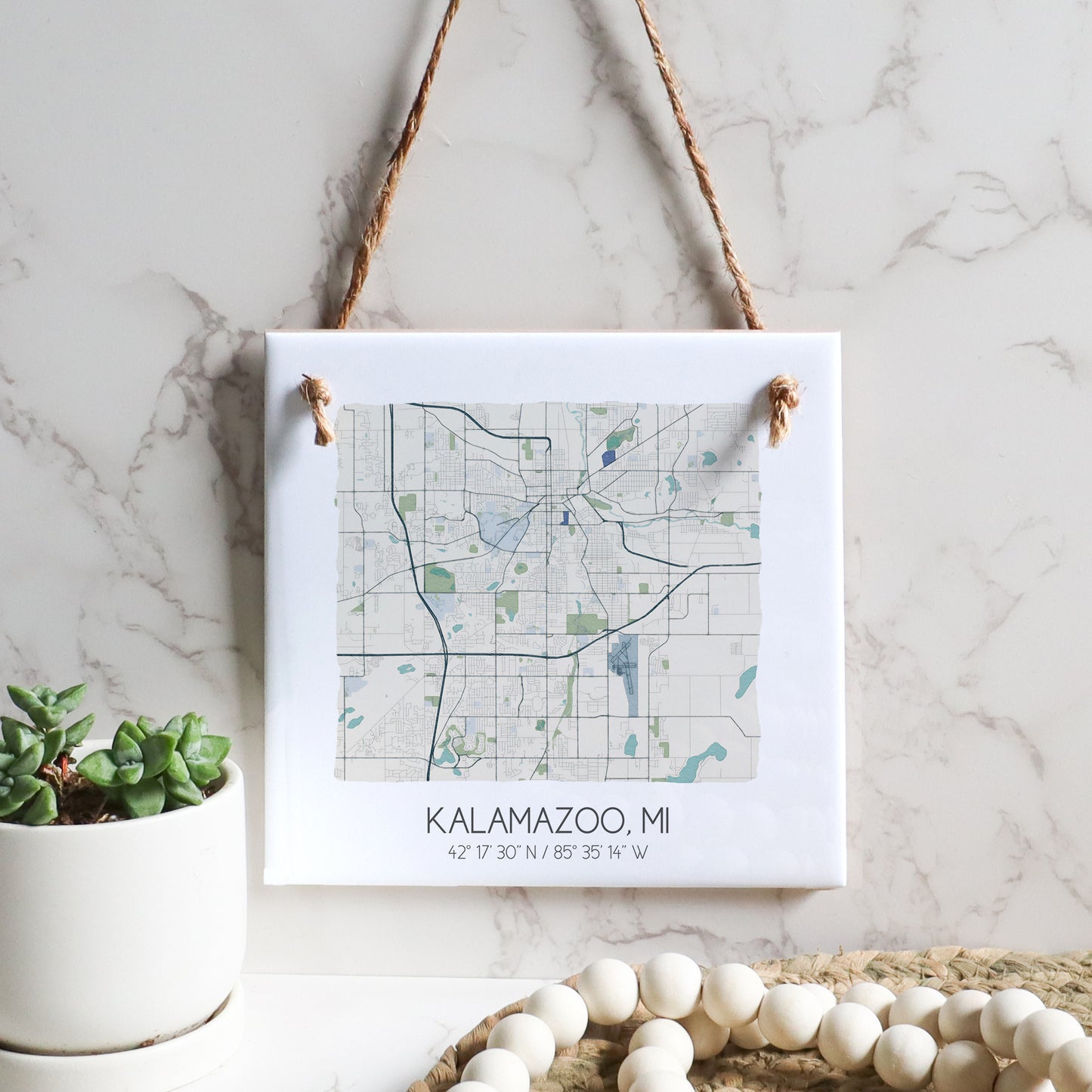 A city map of Kalamazoo MI on a square ceramic tile sign hanging on a wall, in the color beige