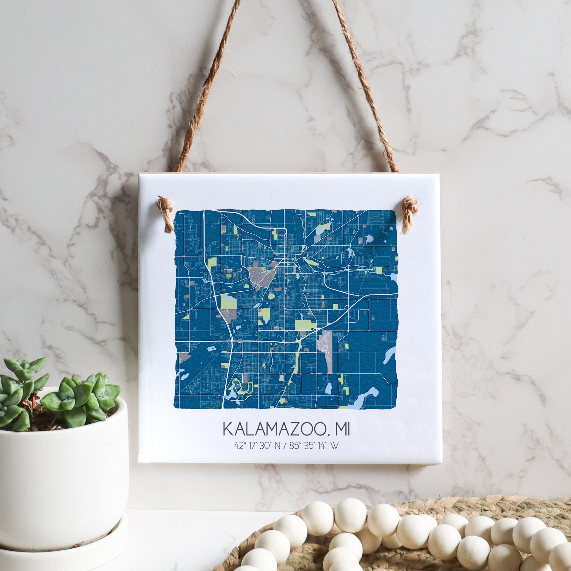 A city map of Kalamazoo MI on a square ceramic tile sign hanging on a wall, in the color blue