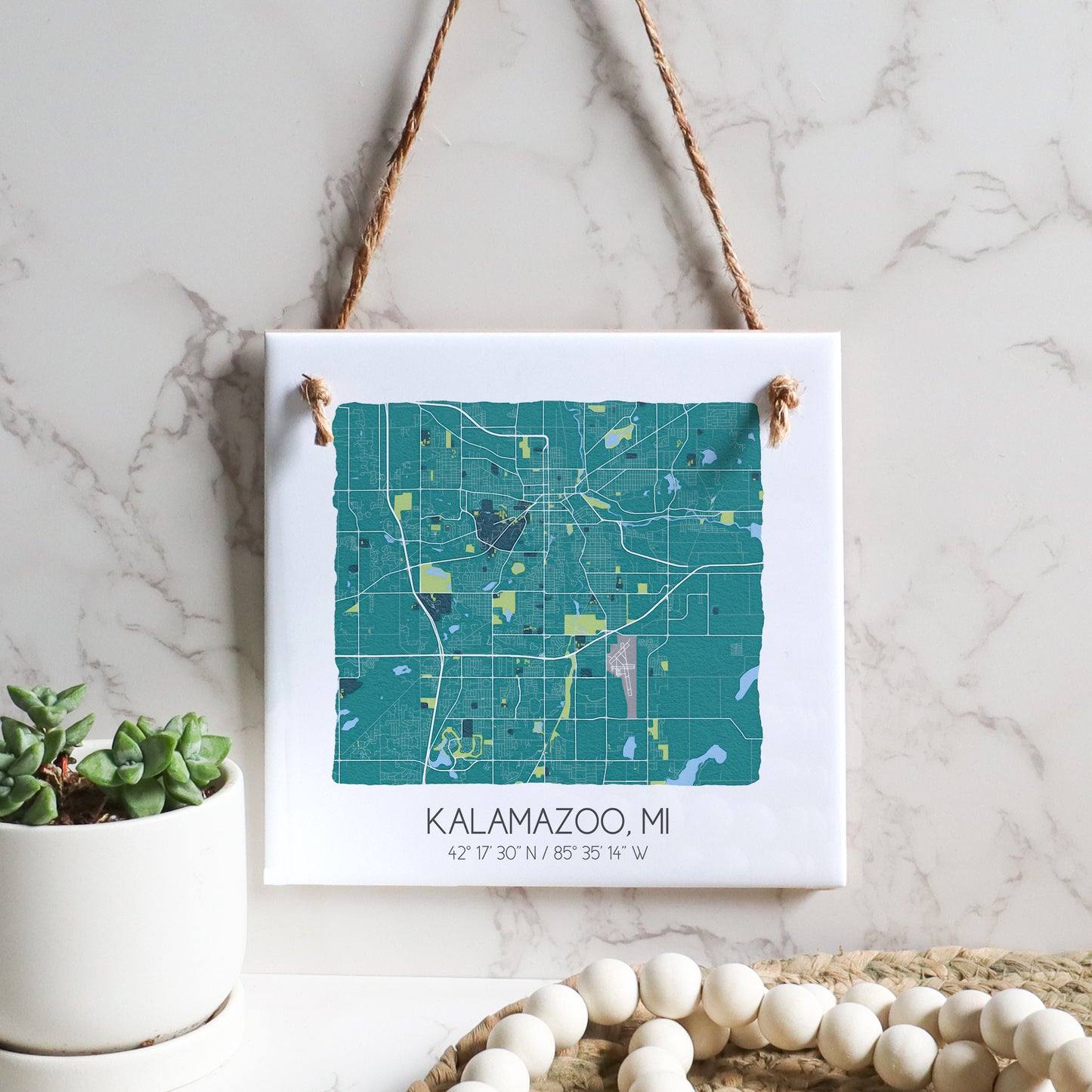 A city map of Kalamazoo MI on a square ceramic tile sign hanging on a wall, in the color teal