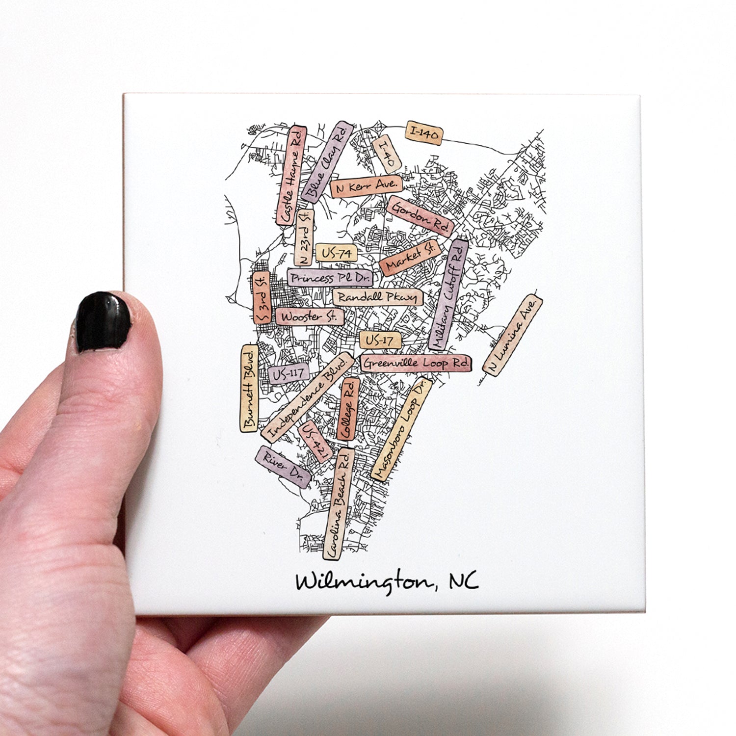 A hand holding a ceramic coaster with a street map of Wilmington NC on it - in the color sunset