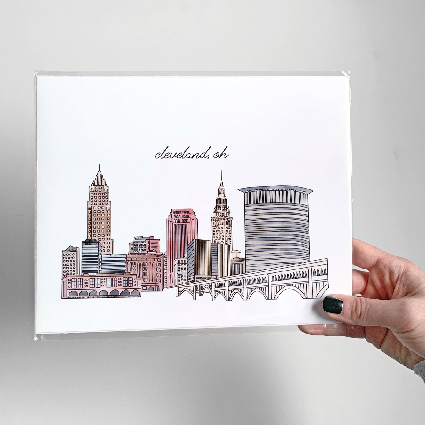 A hand holding a watercolor city skyline print packaged in a clear sleeve.