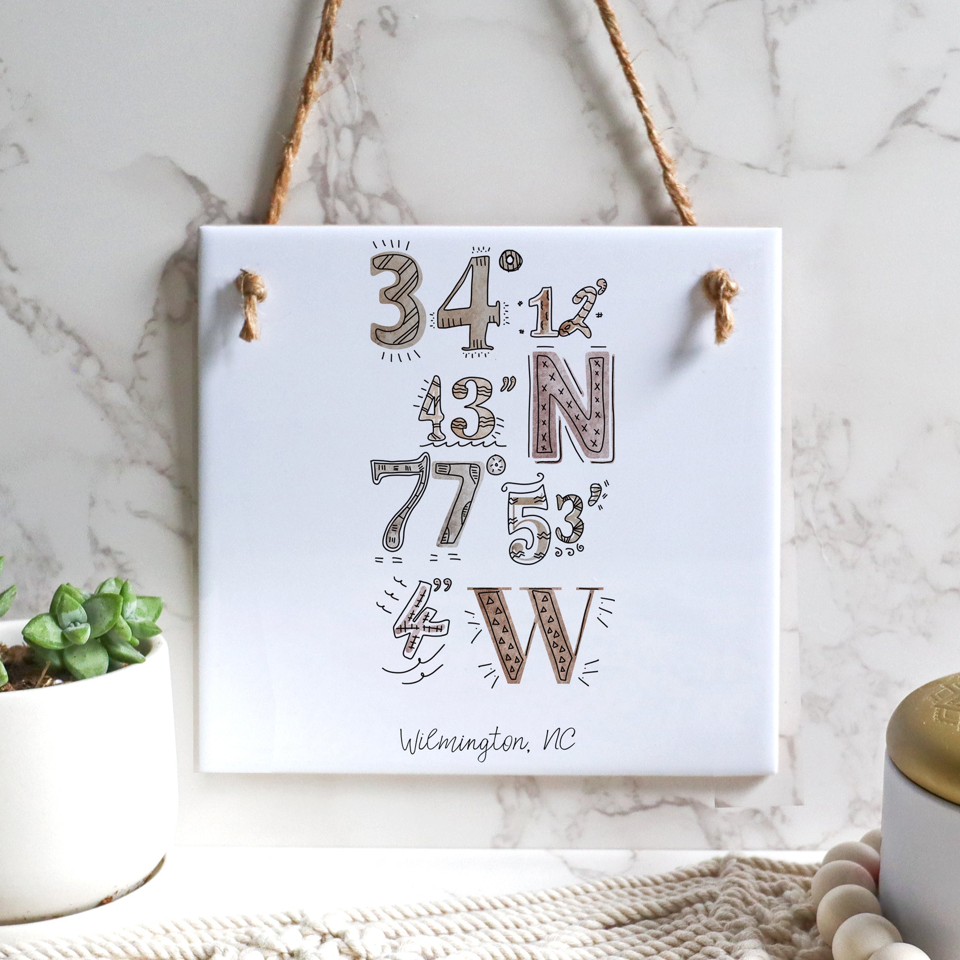 A city art drawing of the Wilmington North Carolina coordinates, on a square tile sign, hanging on a wall - in the color boho