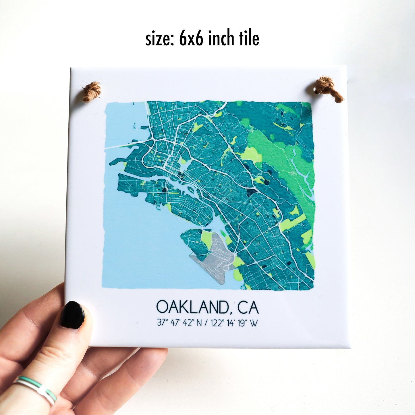 A hand holding a custom city map of a ceramic square tile sign, showing the 6x6 inch size