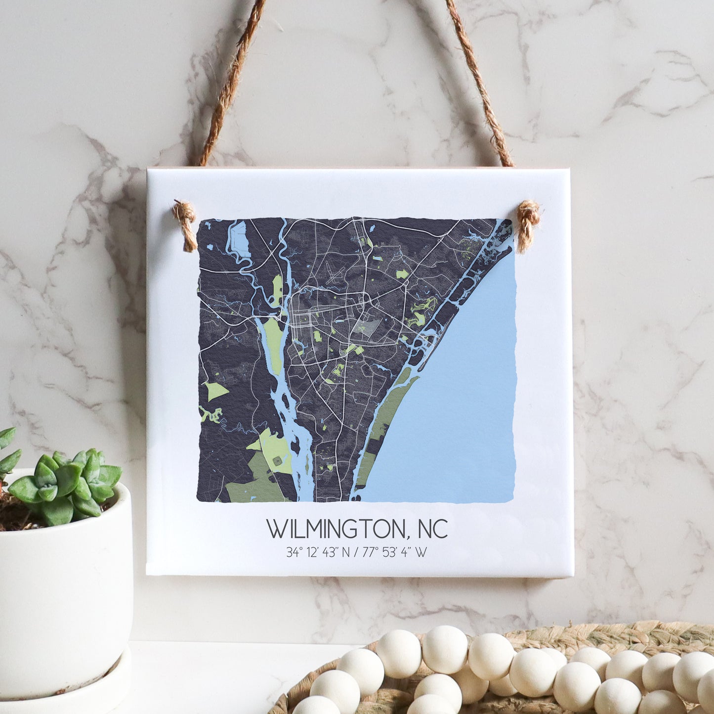 A city map of Wilmington North Carolina on a square ceramic tile sign hanging on a wall, in the color gray