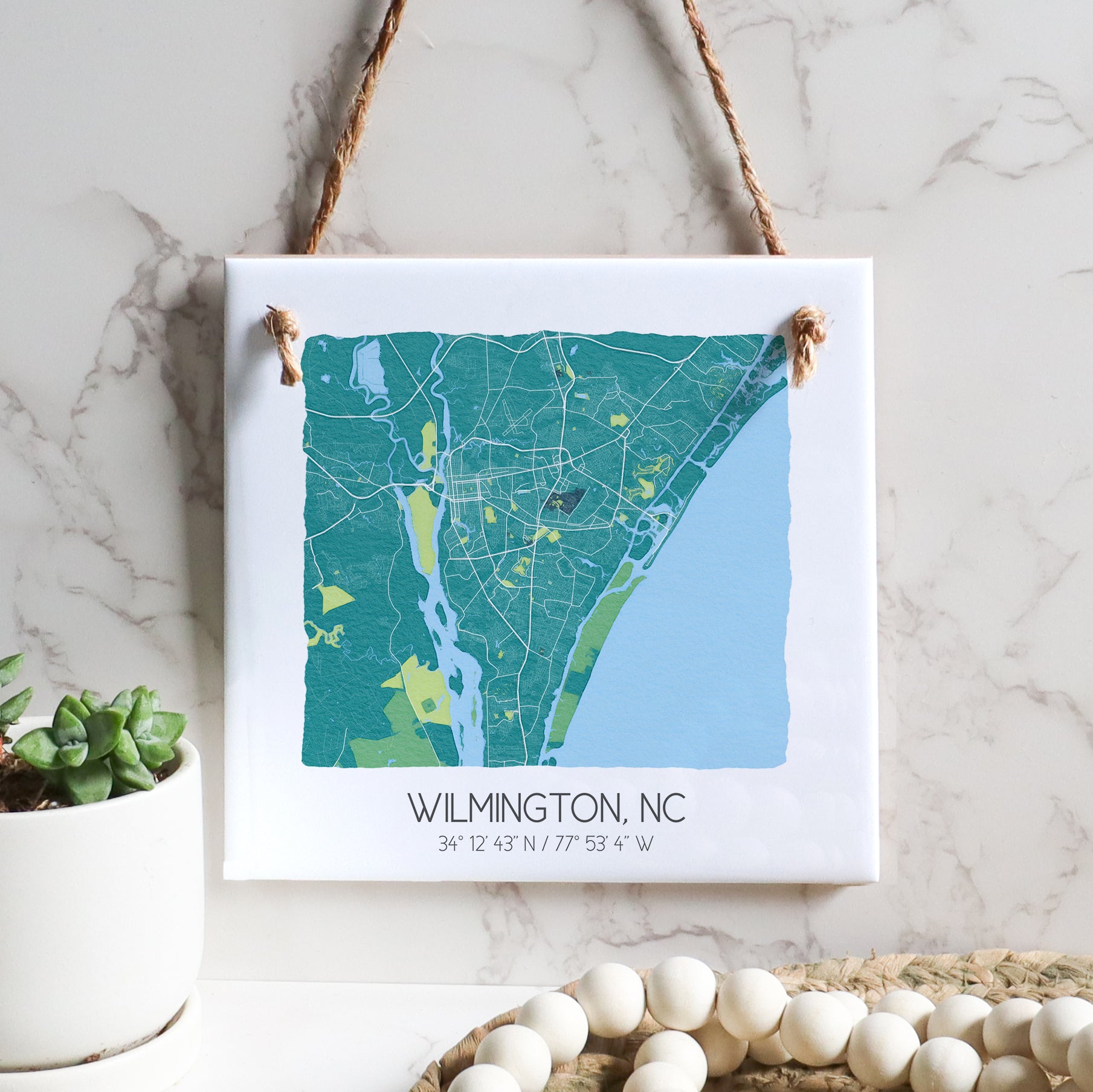 A city map of Wilmington North Carolina on a square ceramic tile sign hanging on a wall, in the color teal