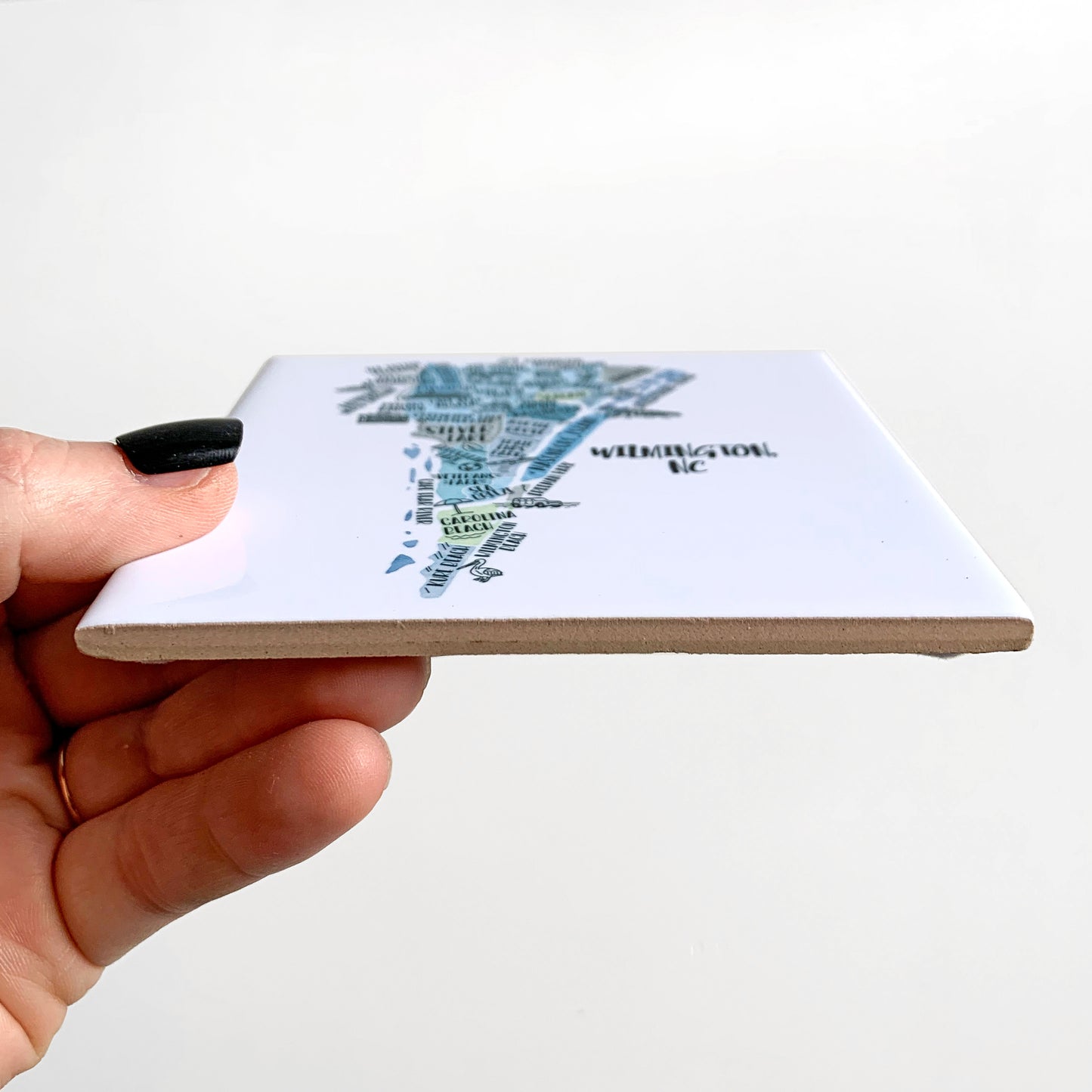 A hand holding a ceramic coaster with a hand-drawn map on it, showing the tile edges