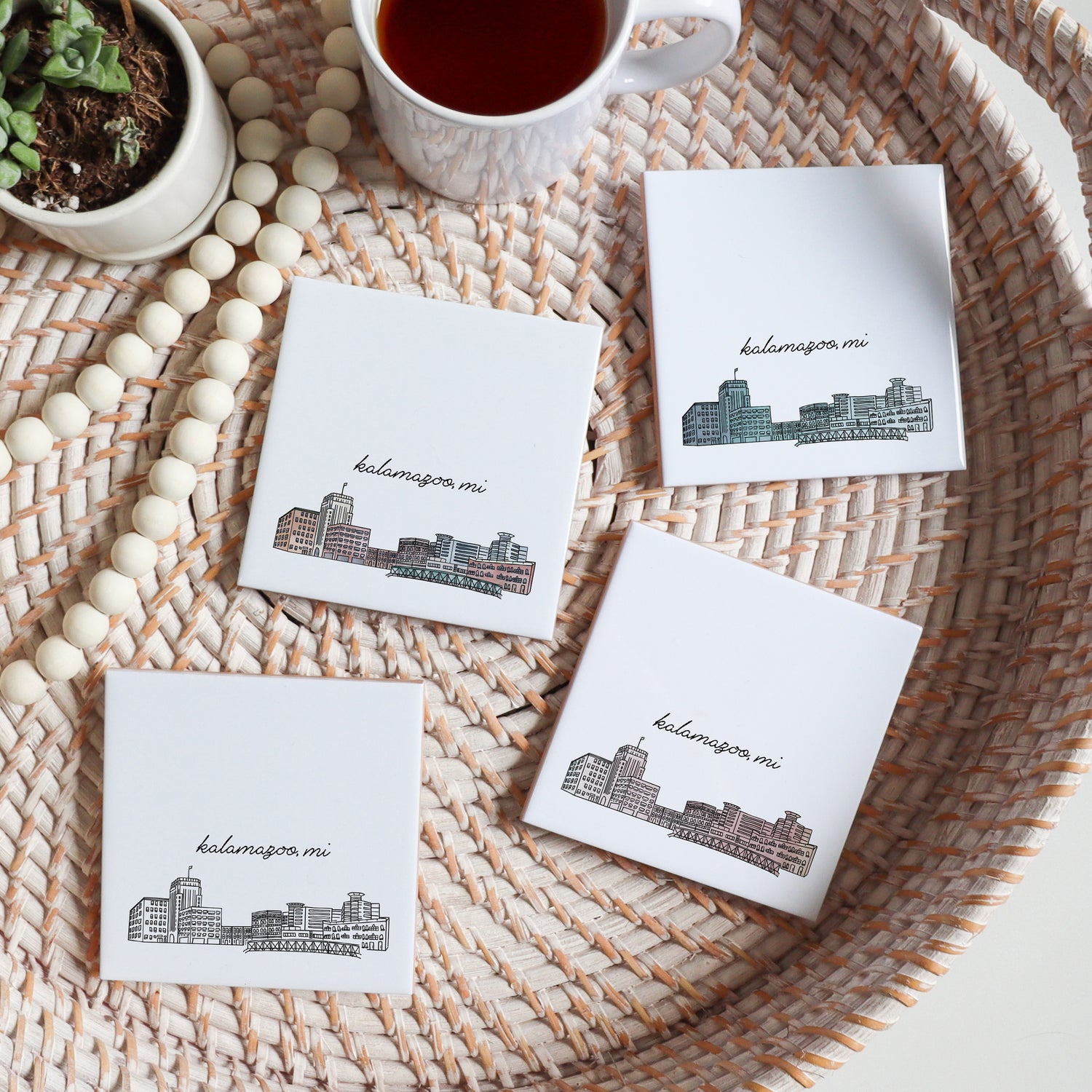Skyline drawing of Kalamazoo Michigan on a set of ceramic coasters sitting on a serving tray with a cup of tea