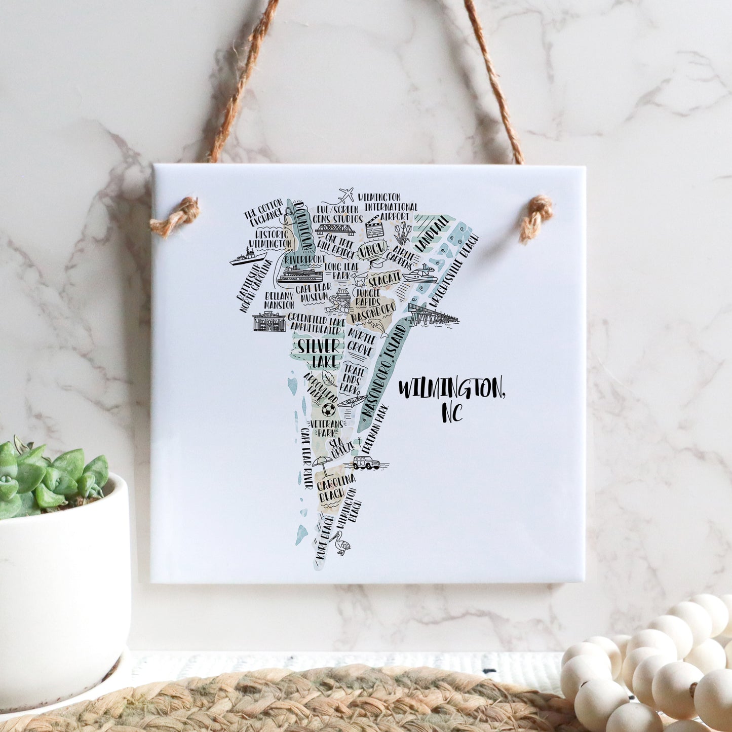A hand-drawn tourist map of Wilmington North Carolina on a square tile sign hanging on a wall - in the color beige