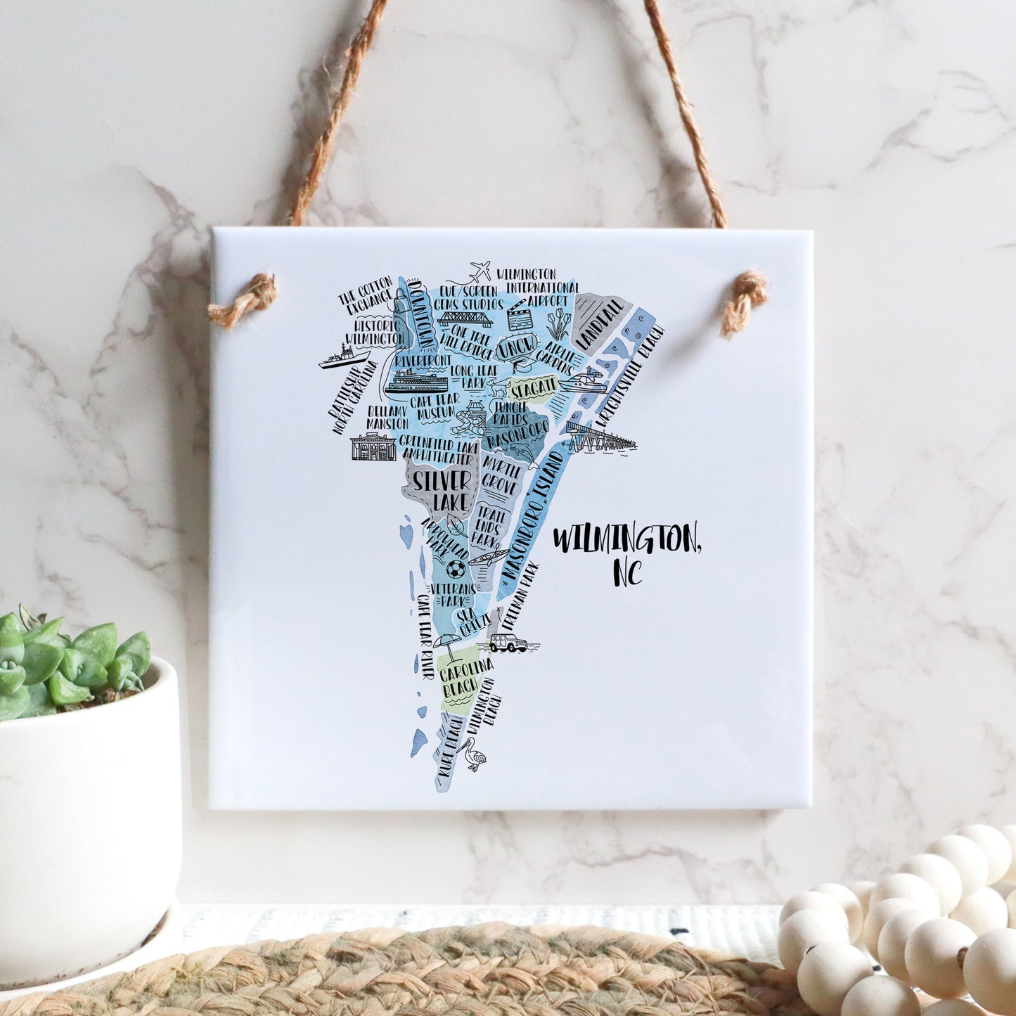 A hand-drawn tourist map of Wilmington North Carolina on a square tile sign hanging on a wall - in the color blue
