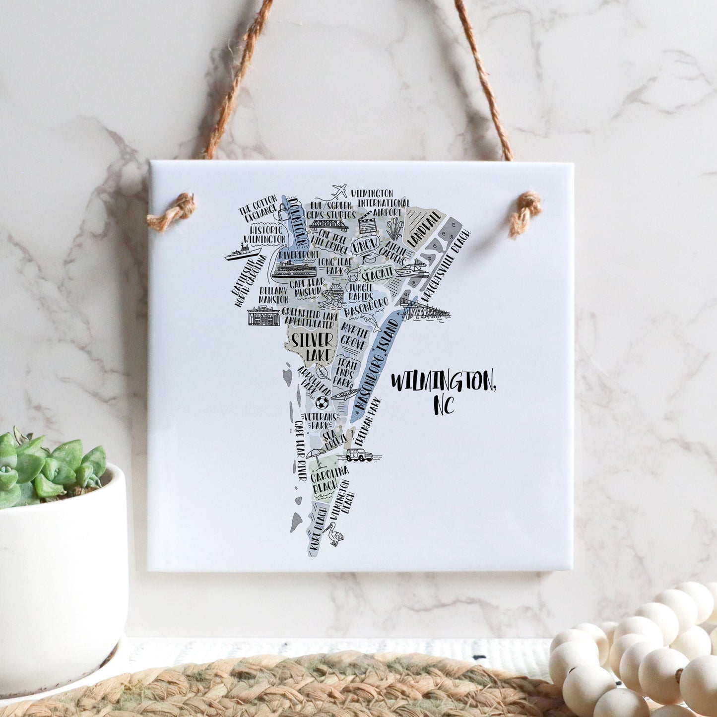 A hand-drawn tourist map of Wilmington North Carolina on a square tile sign hanging on a wall - in the color gray