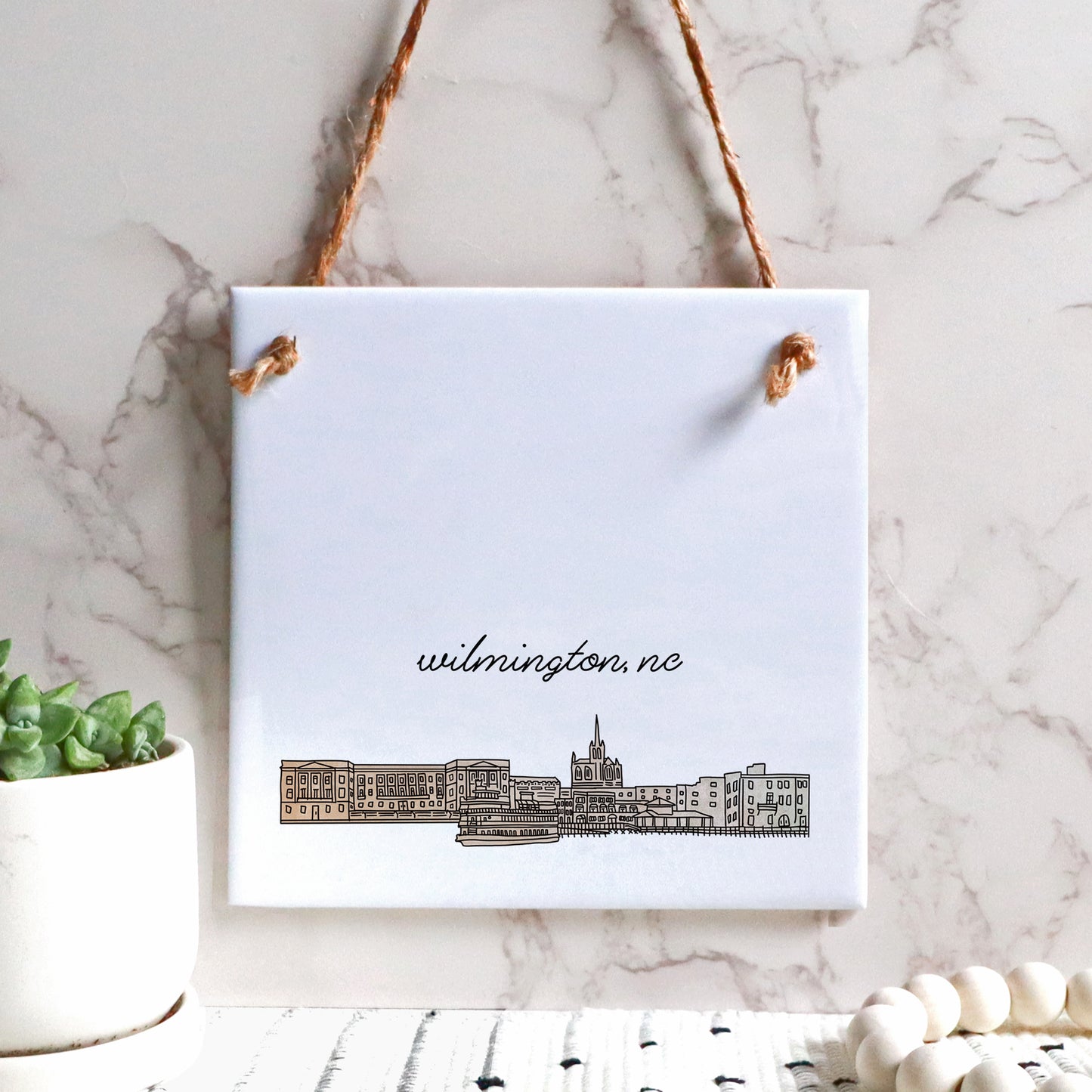 A hand drawn city drawing of Wilmington NC, on ceramic square tile sign, hanging on a wall - in the color beige