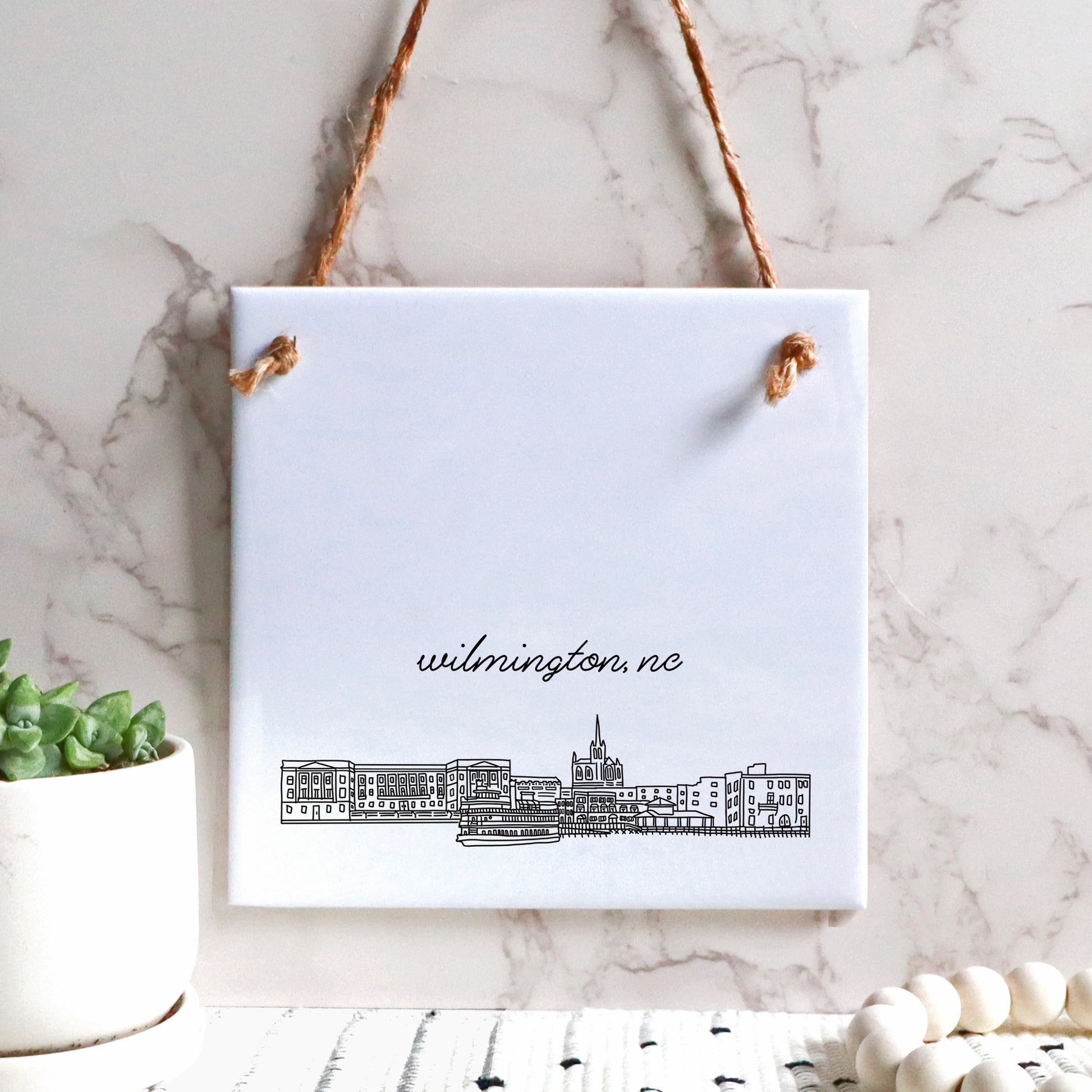 A hand drawn city drawing of Wilmington NC, on ceramic square tile sign, hanging on a wall - in the color black and white