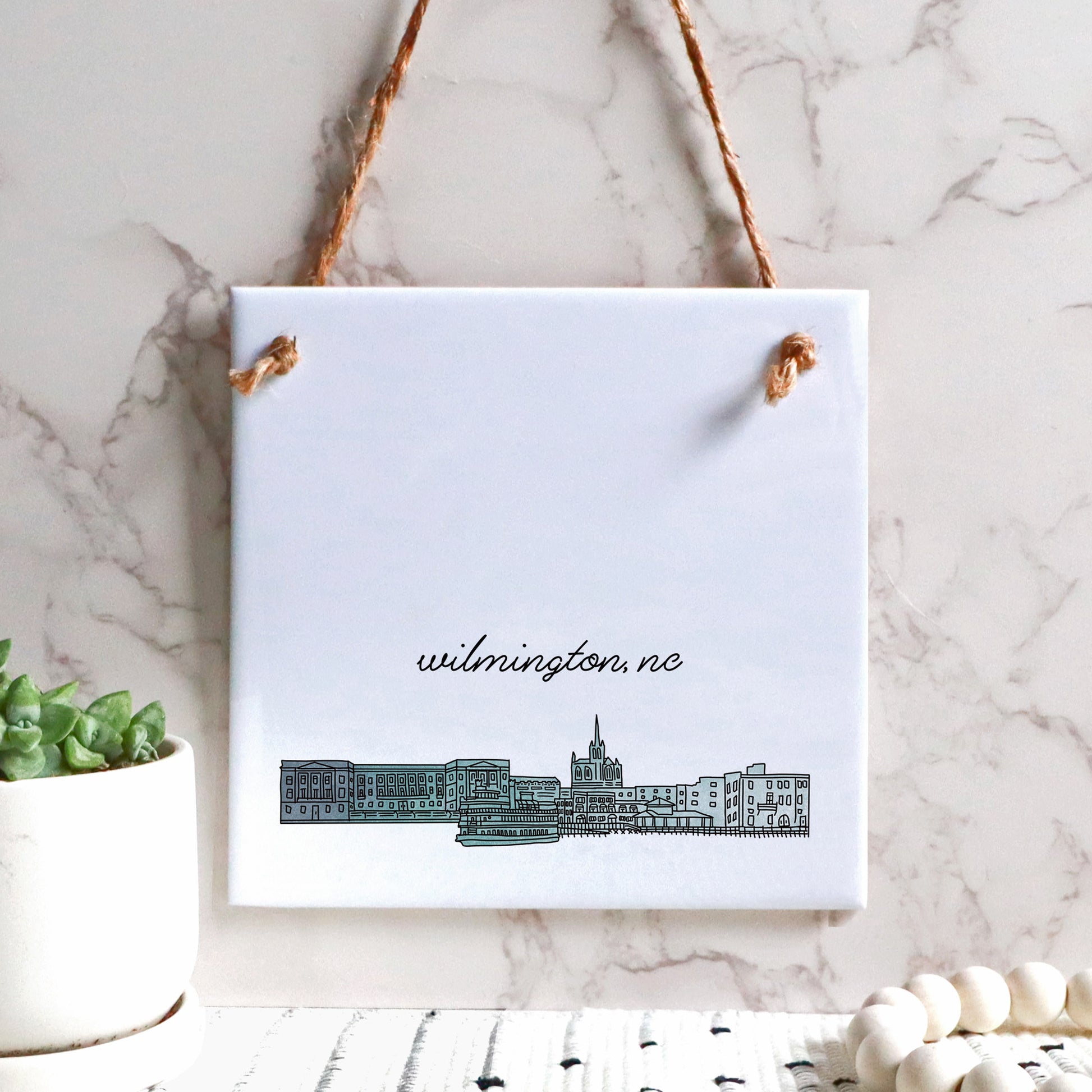 A hand drawn city drawing of Wilmington NC, on ceramic square tile sign, hanging on a wall - in the color blue