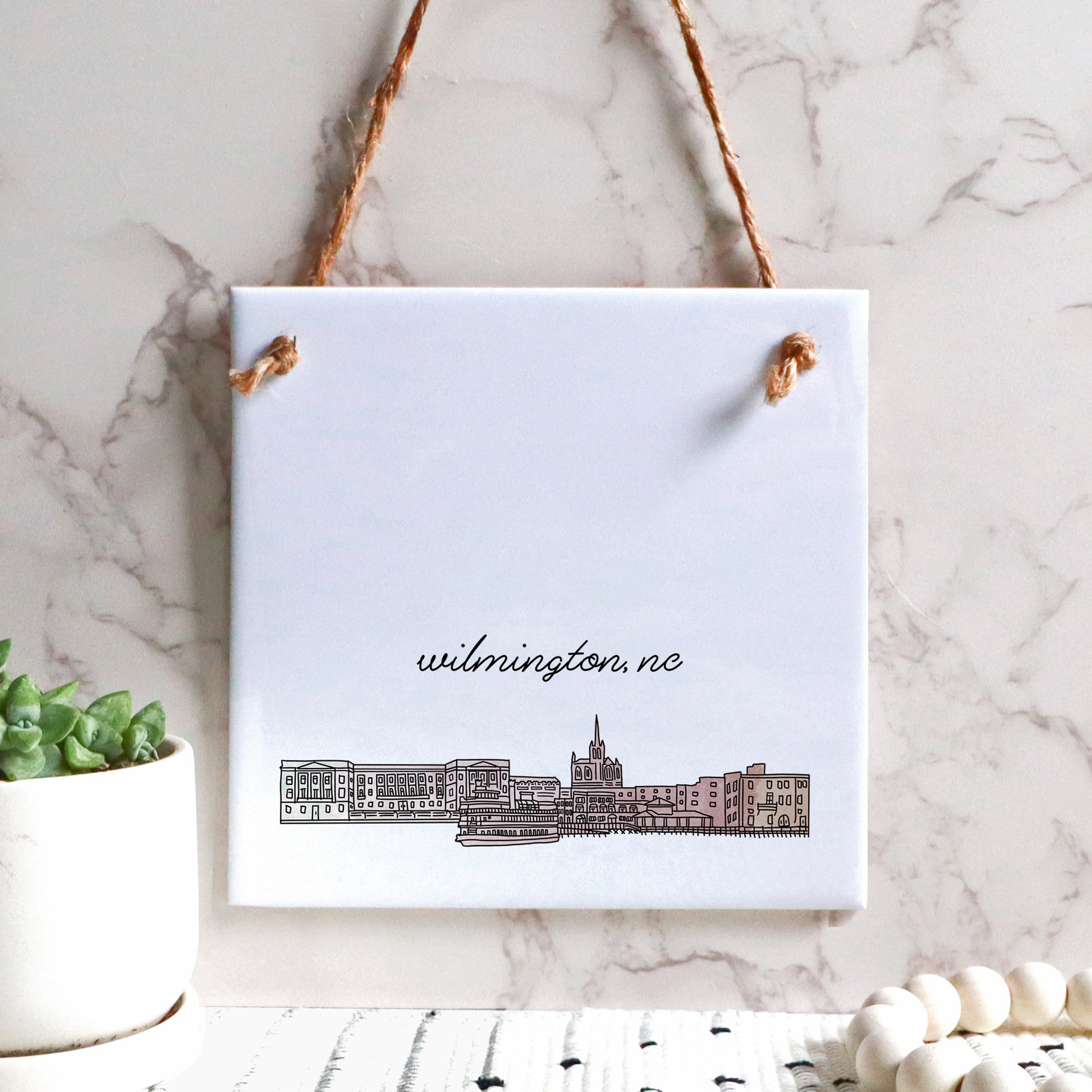 A hand drawn city drawing of Wilmington NC, on ceramic square tile sign, hanging on a wall - in the color blush