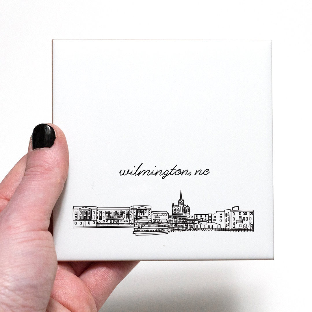 A hand holding a ceramic coaster with a city drawing of Wilmington NC - in the color black and white
