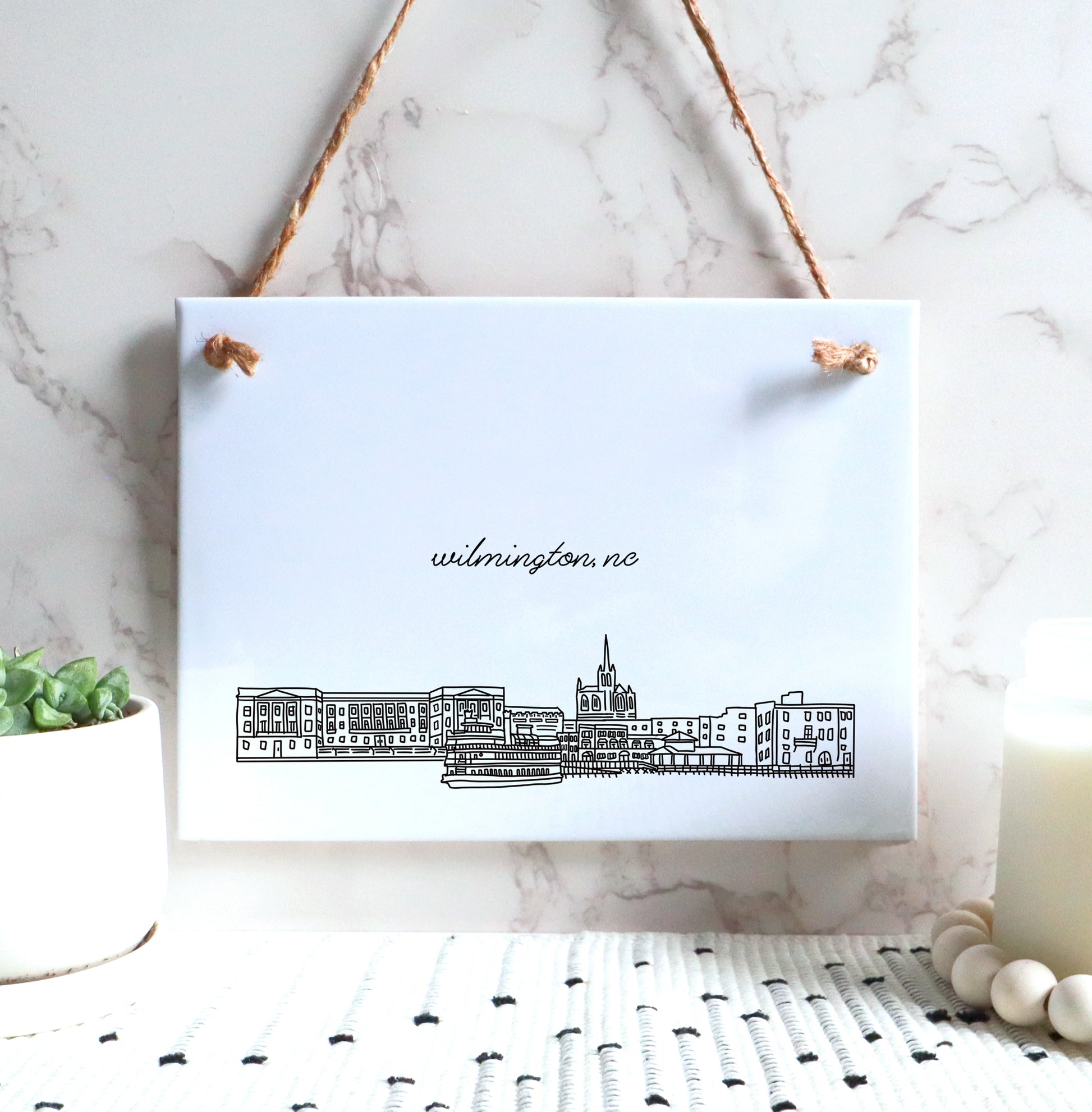 A Wilmington NC souvenir of a drawing of the city skyline on a rectangle tile sign, in the color black and white