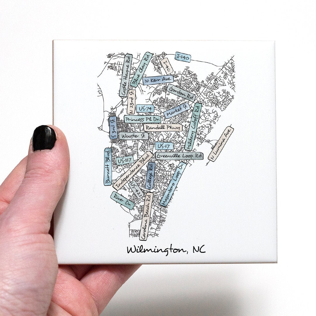 A hand holding a ceramic coaster with a street map of Wilmington NC on it - in the color coastal