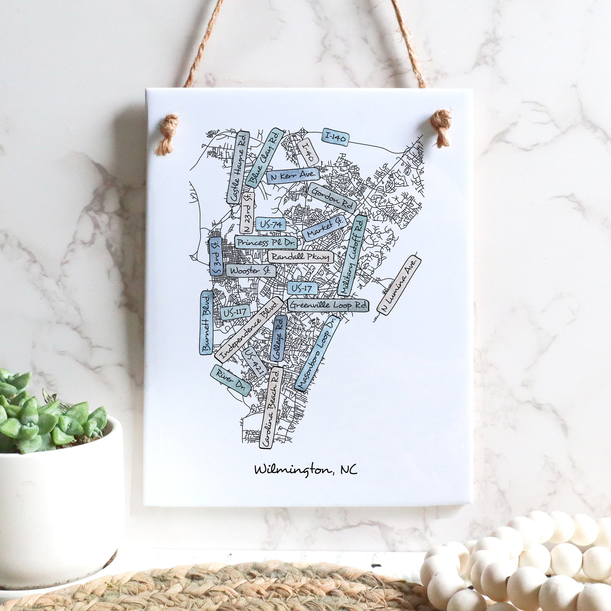 A street map drawing of Wilmington NC on a rectangle tile sign hanging on a wall - in the color coastal