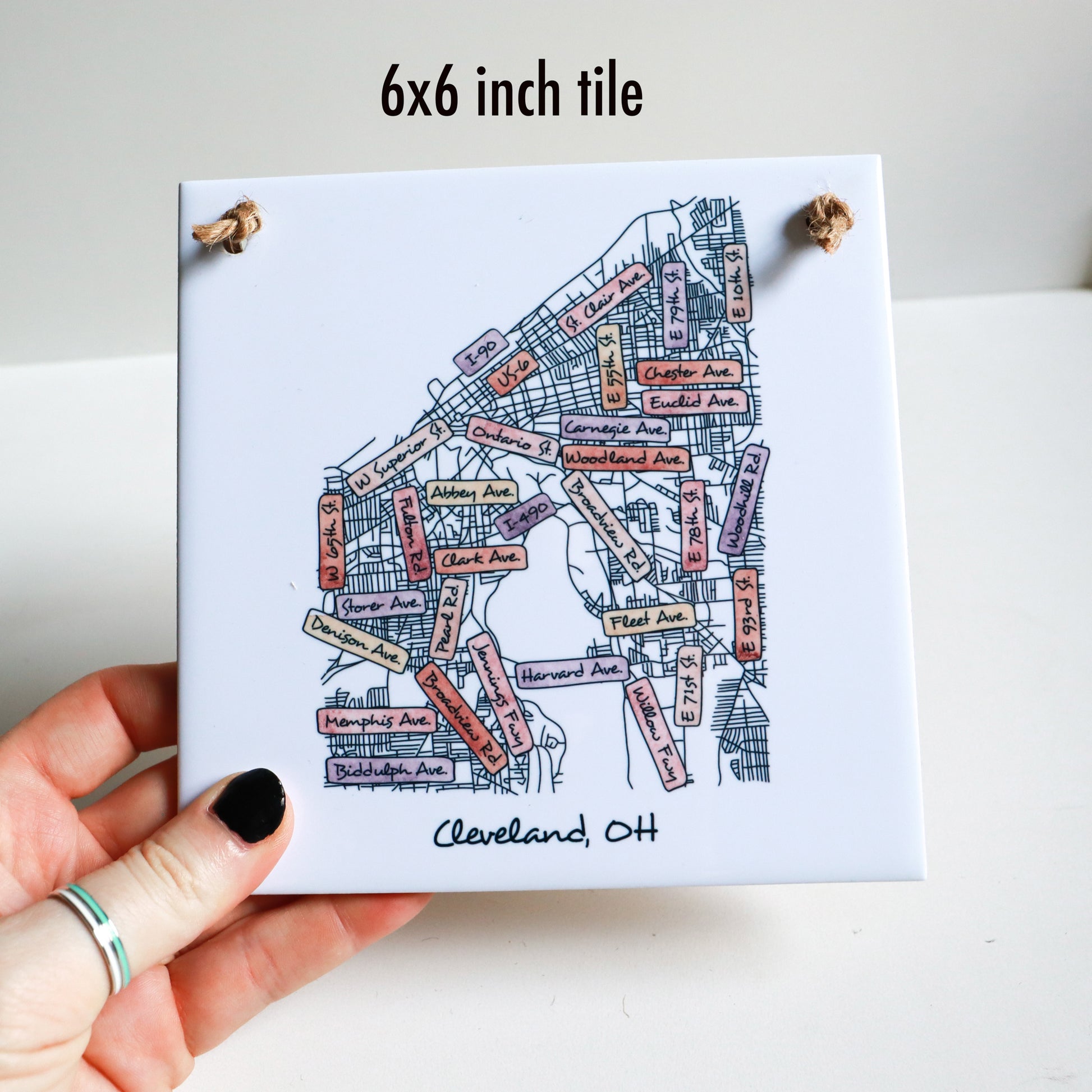 A hand holding a custom city street map drawing on a square tile sign, showing the 6x6 inch size