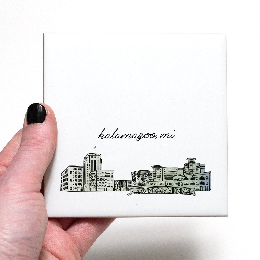 A hand holding a ceramic coaster with a city drawing of Kalamazoo MI - in the color green