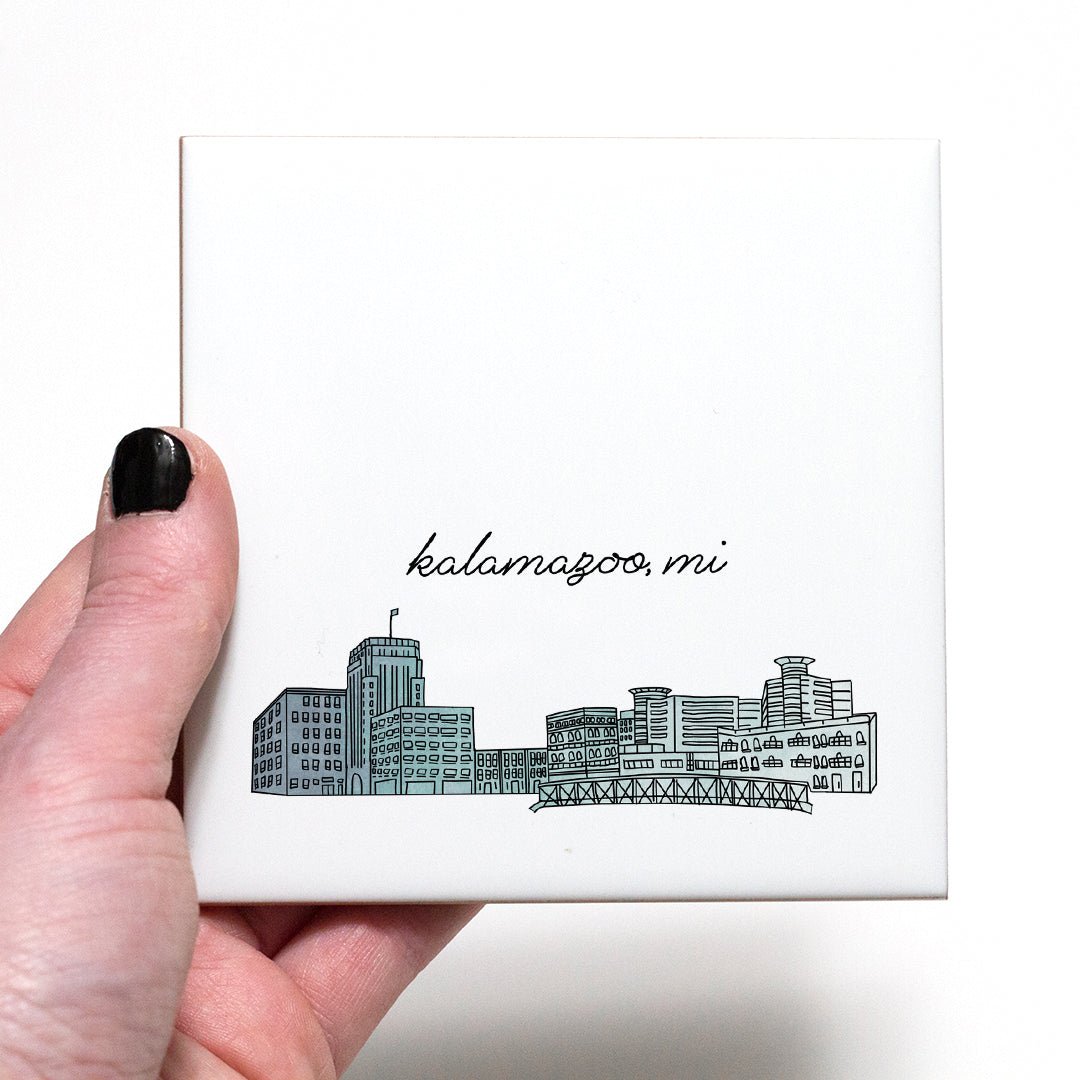 A hand holding a ceramic coaster with a city drawing of Kalamazoo MI - in the color blue