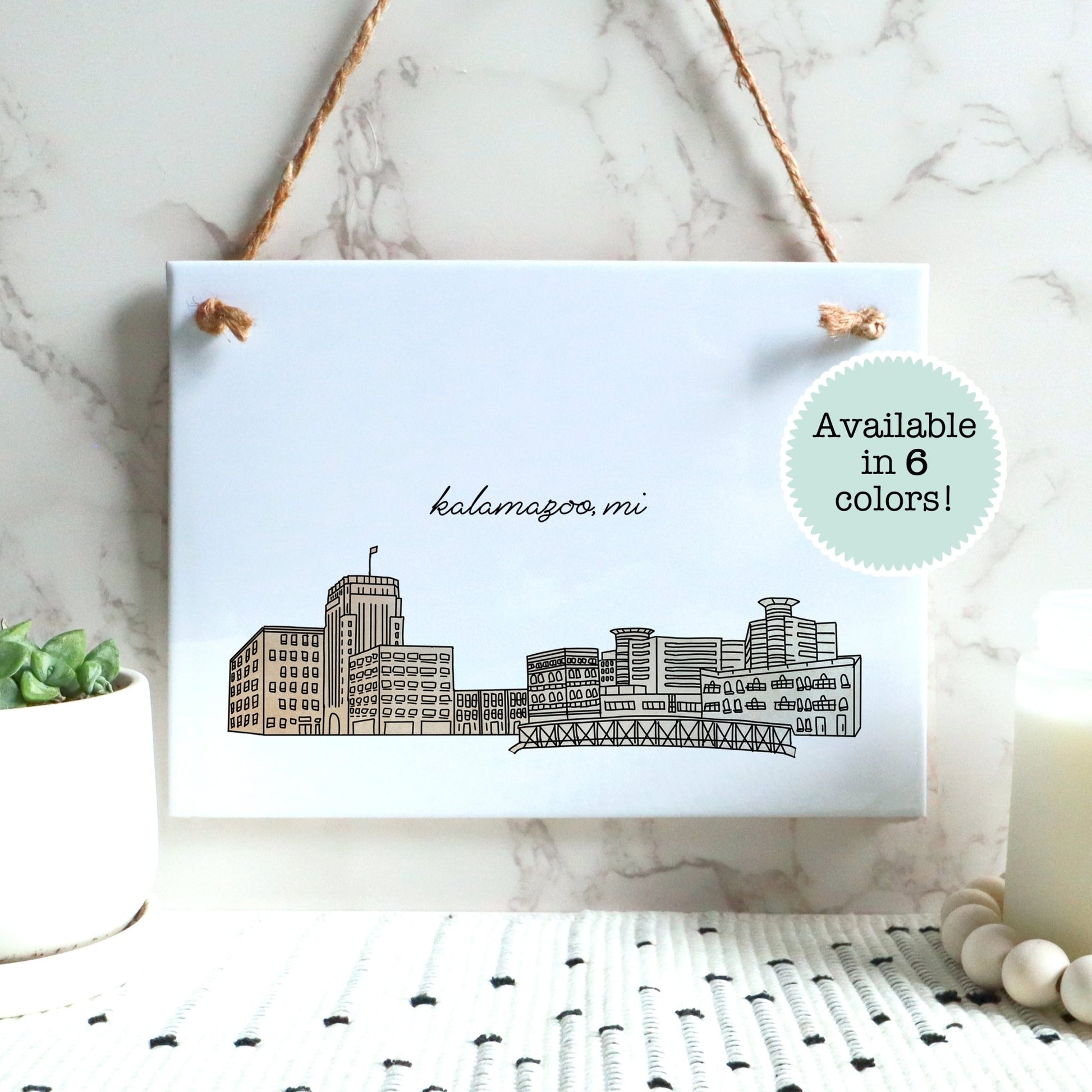 A Kalamazoo MI souvenir of a drawing of the city skyline on a rectangle tile sign, hanging on a wall - in the color beige
