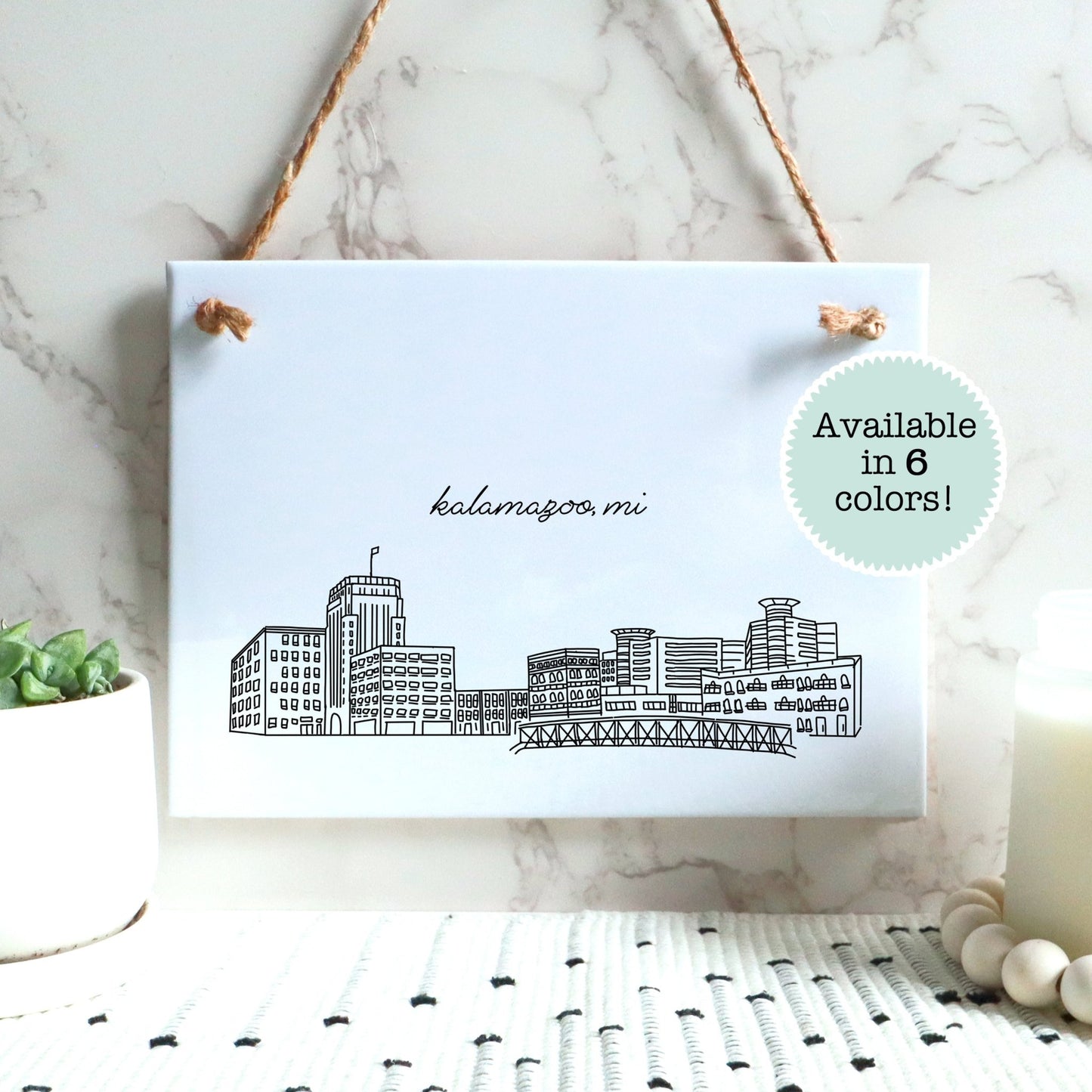 A Kalamazoo MI souvenir of a drawing of the city skyline on a rectangle tile sign, hanging on a wall - in black and white