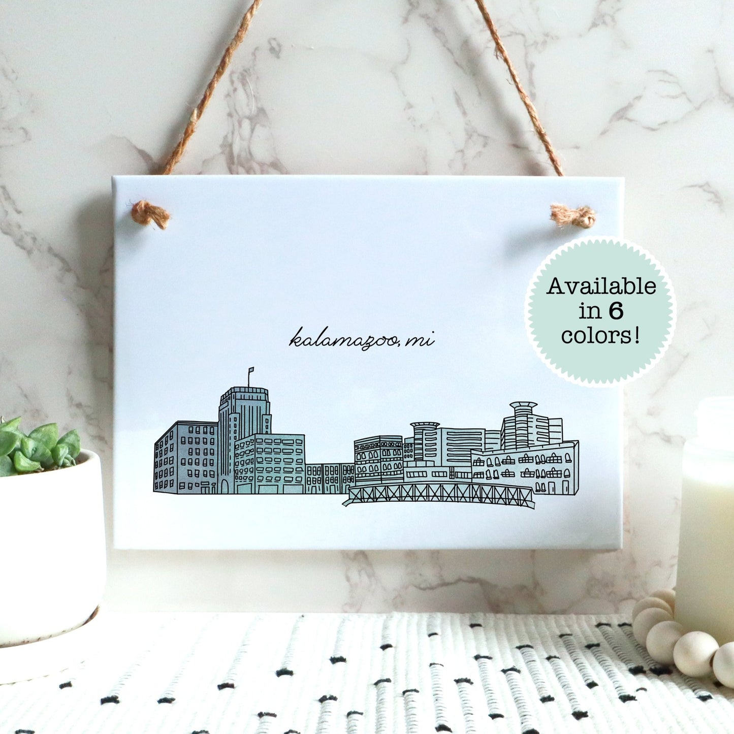 A Kalamazoo MI souvenir of a drawing of the city skyline on a rectangle tile sign, hanging on a wall - in the color blue