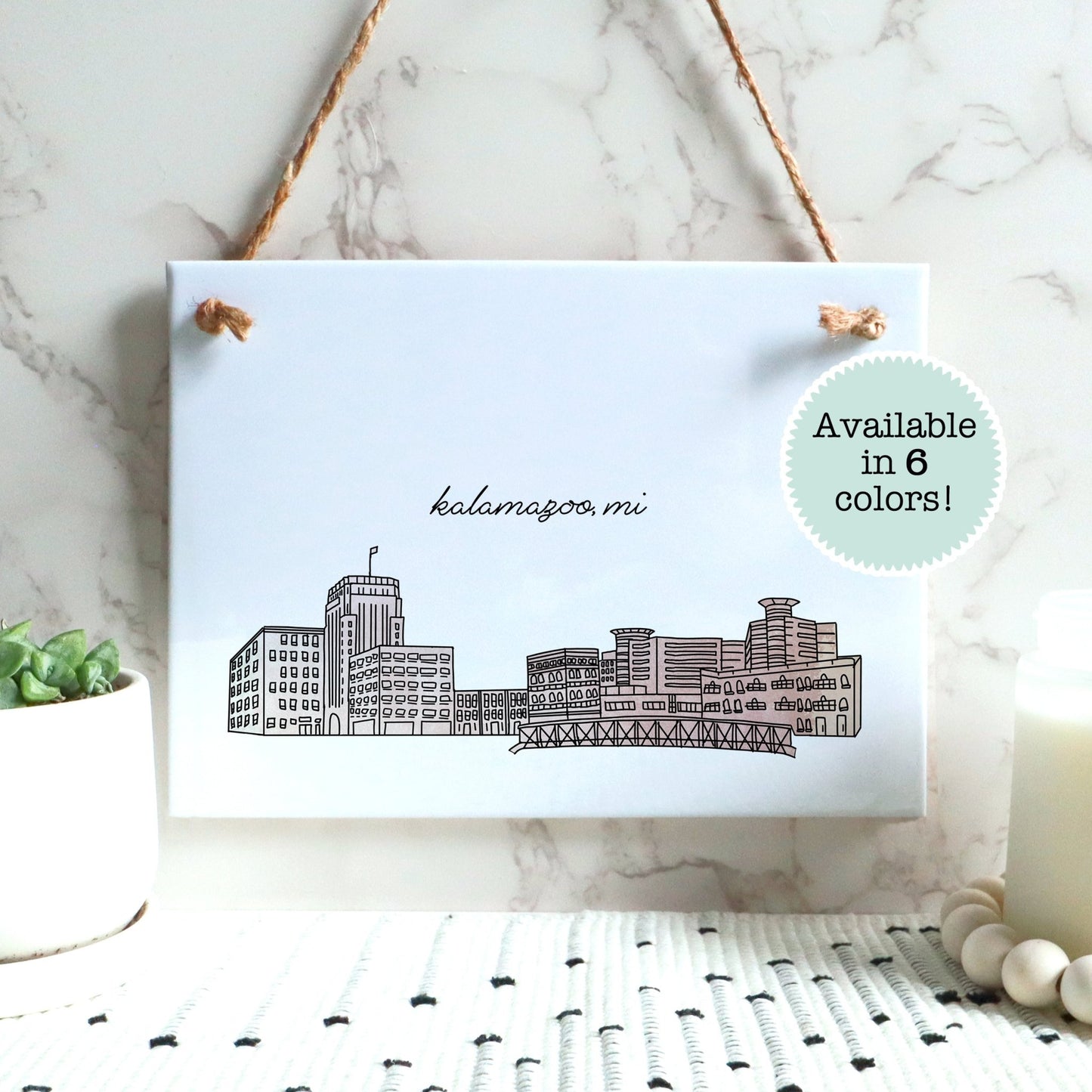 A Kalamazoo MI souvenir of a drawing of the city skyline on a rectangle tile sign, hanging on a wall - in the color blush
