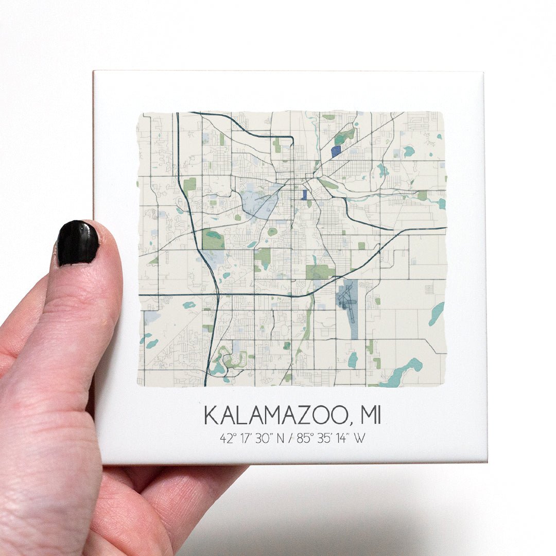 A hand holding a ceramic map coaster of Kalamazoo MI - in the color beige