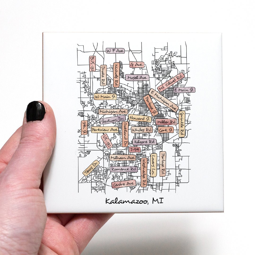 A hand holding a ceramic coaster with a street map of Kalamazoo MI on it - in the color sunset