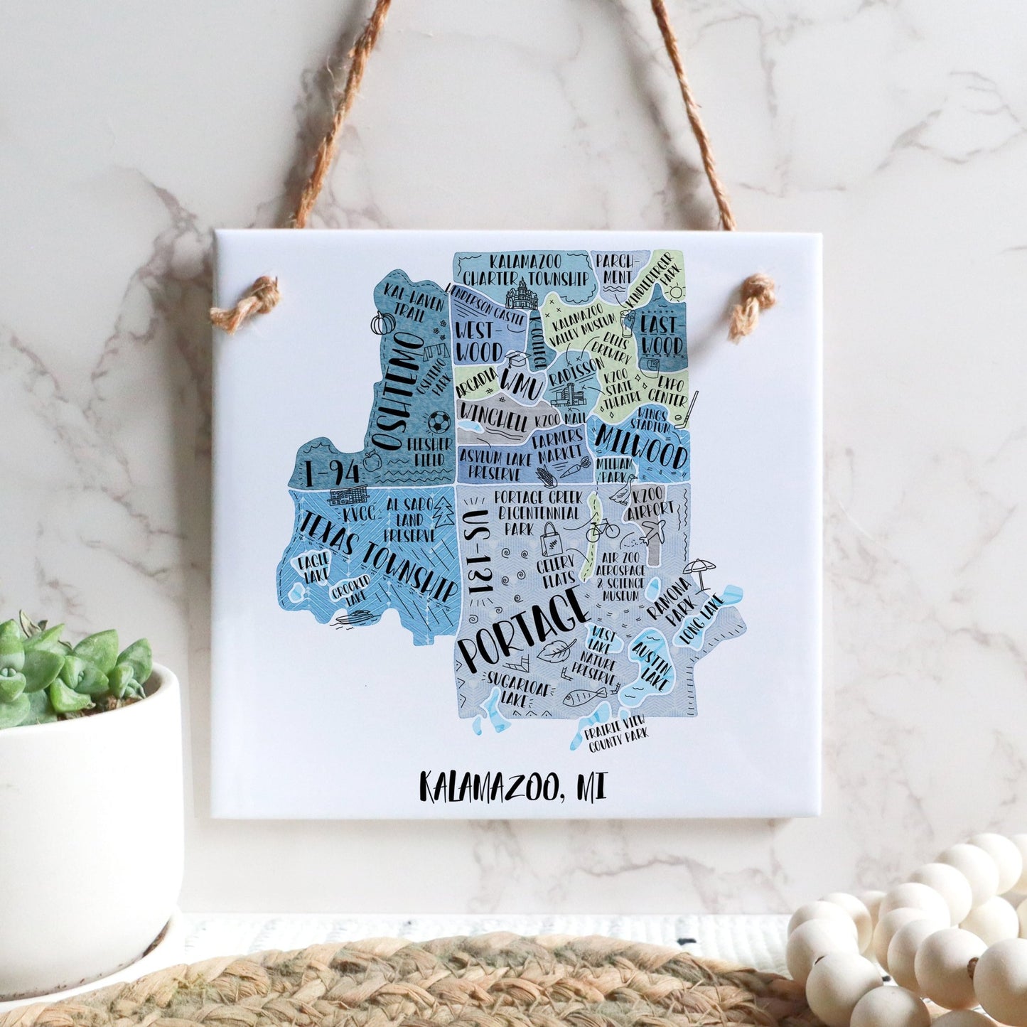 A hand-drawn tourist map of Kalamazoo MI on a square tile sign hanging on a wall - in the color blue