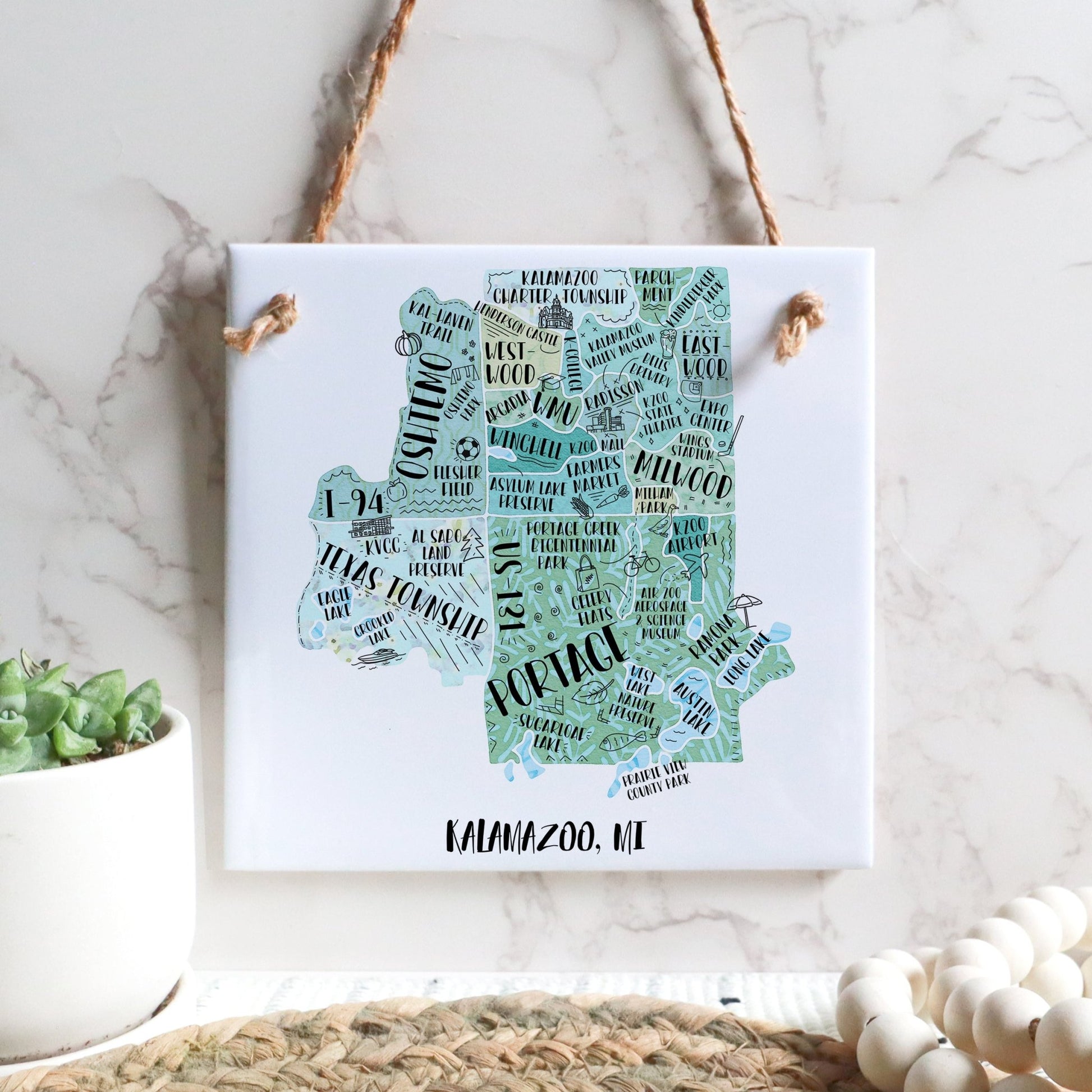 A hand-drawn tourist map of Kalamazoo MI on a square tile sign hanging on a wall - in the color teal
