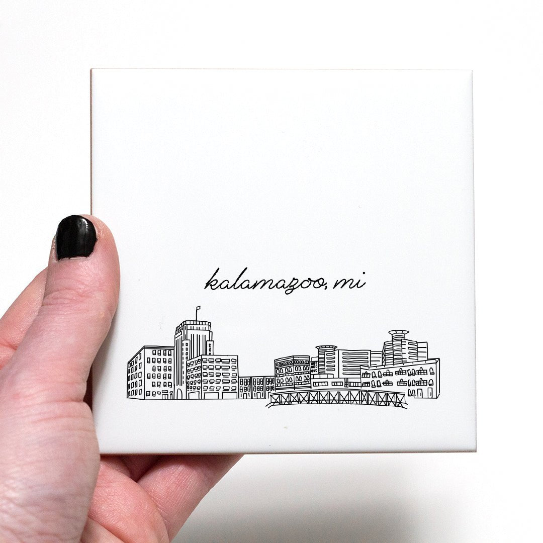 A hand holding a ceramic coaster with a city drawing of Kalamazoo MI - in the color black and white