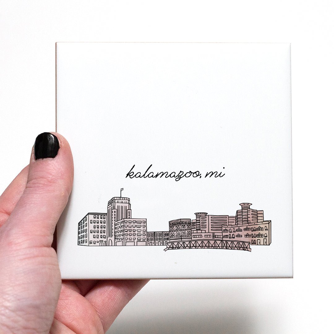 A hand holding a ceramic coaster with a city drawing of Kalamazoo MI - in the color blush