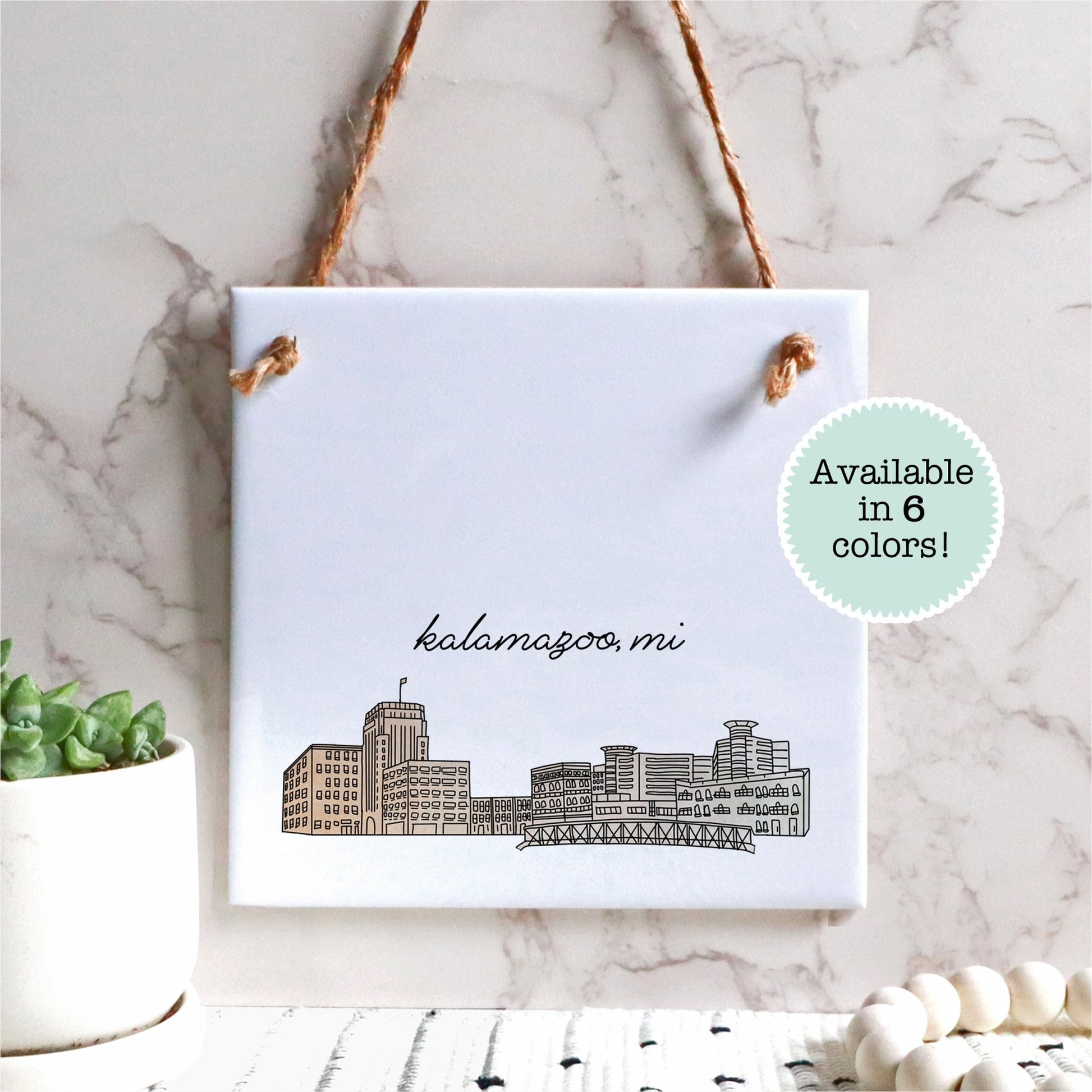 A hand drawn city drawing of Kalamazoo MI, on ceramic square tile sign, hanging on a wall - in the color beige