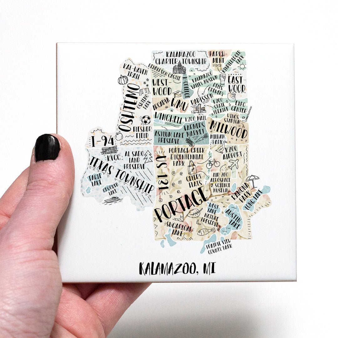A hand holding a coaster with an illustrated map of Kalamazoo MI on it - in the color beige