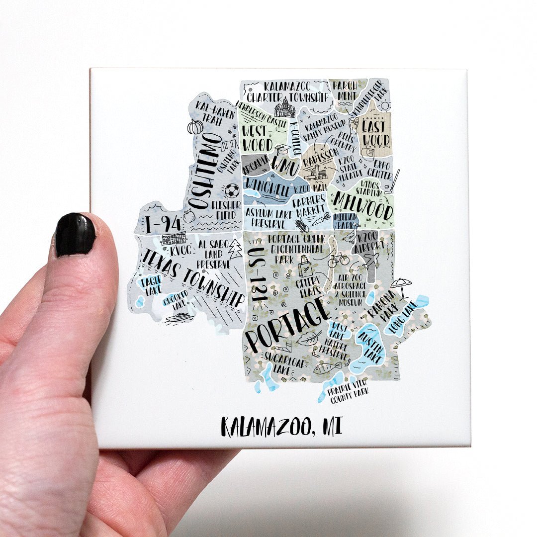 A hand holding a coaster with an illustrated map of Kalamazoo MI on it - in the color gray