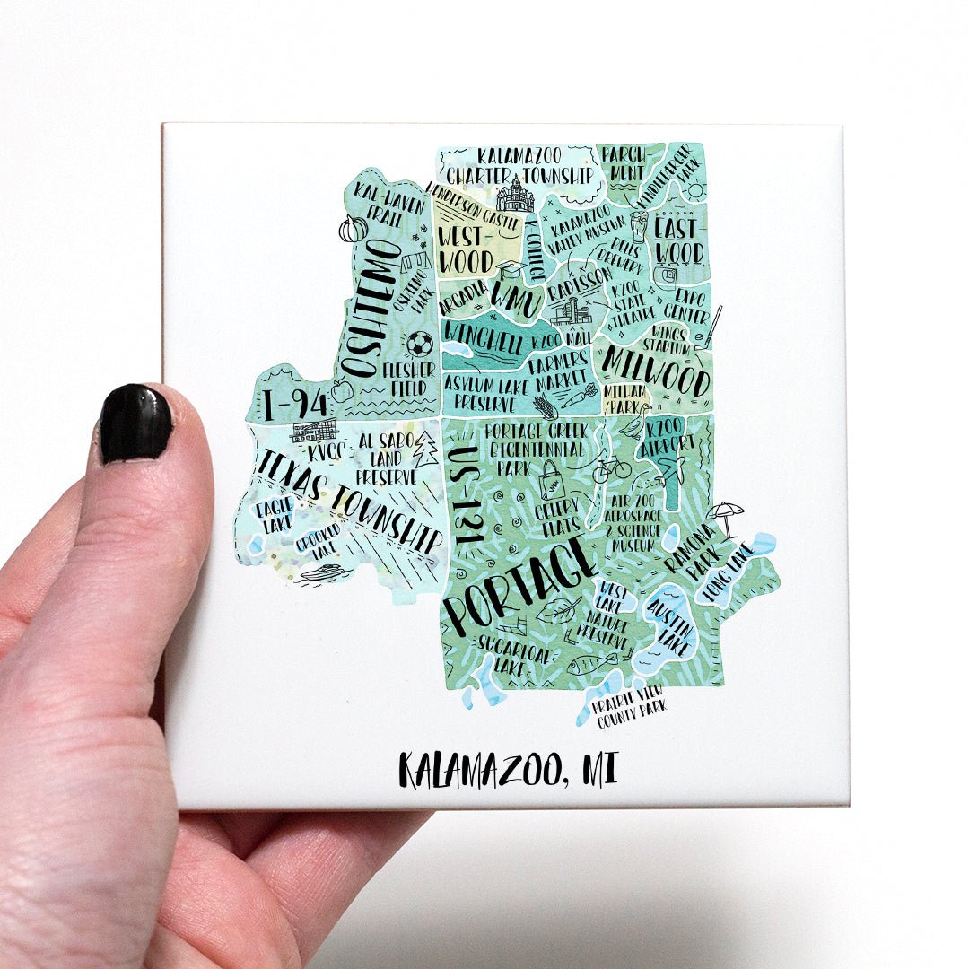 A hand holding a coaster with an illustrated map of Kalamazoo MI on it - in the color teal