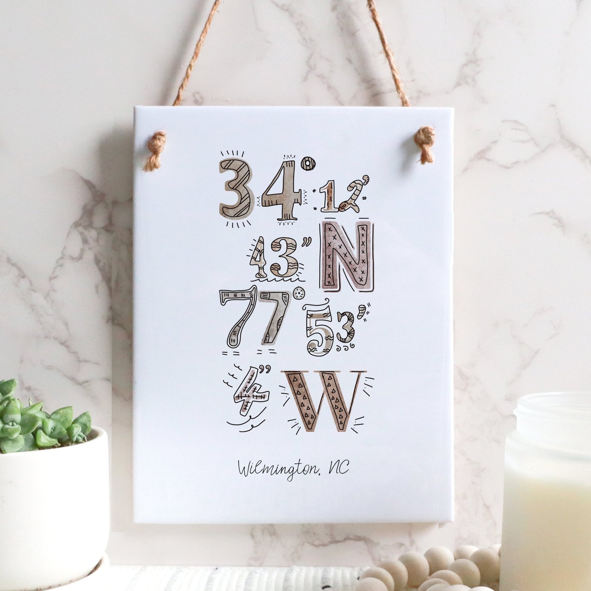 A city drawing of the coordinates of Wilmington NC on a rectangle tile sign, hanging on a wall, in the color boho