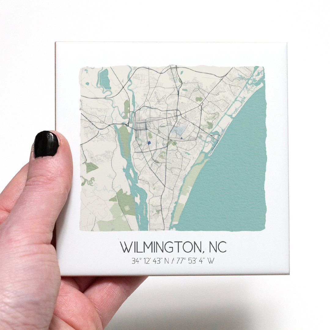 A hand holding a ceramic map coaster of Wilmington NC - in the color beige