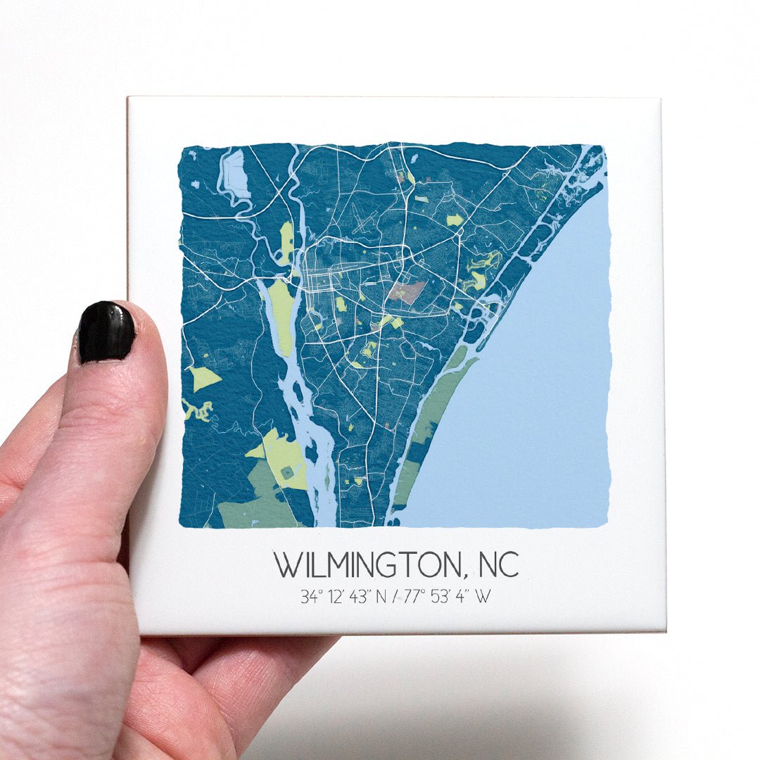 A hand holding a ceramic map coaster of Wilmington NC - in the color blue
