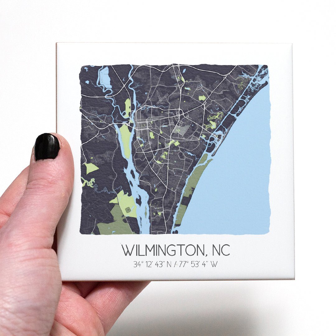 A hand holding a ceramic map coaster of Wilmington NC - in the color gray