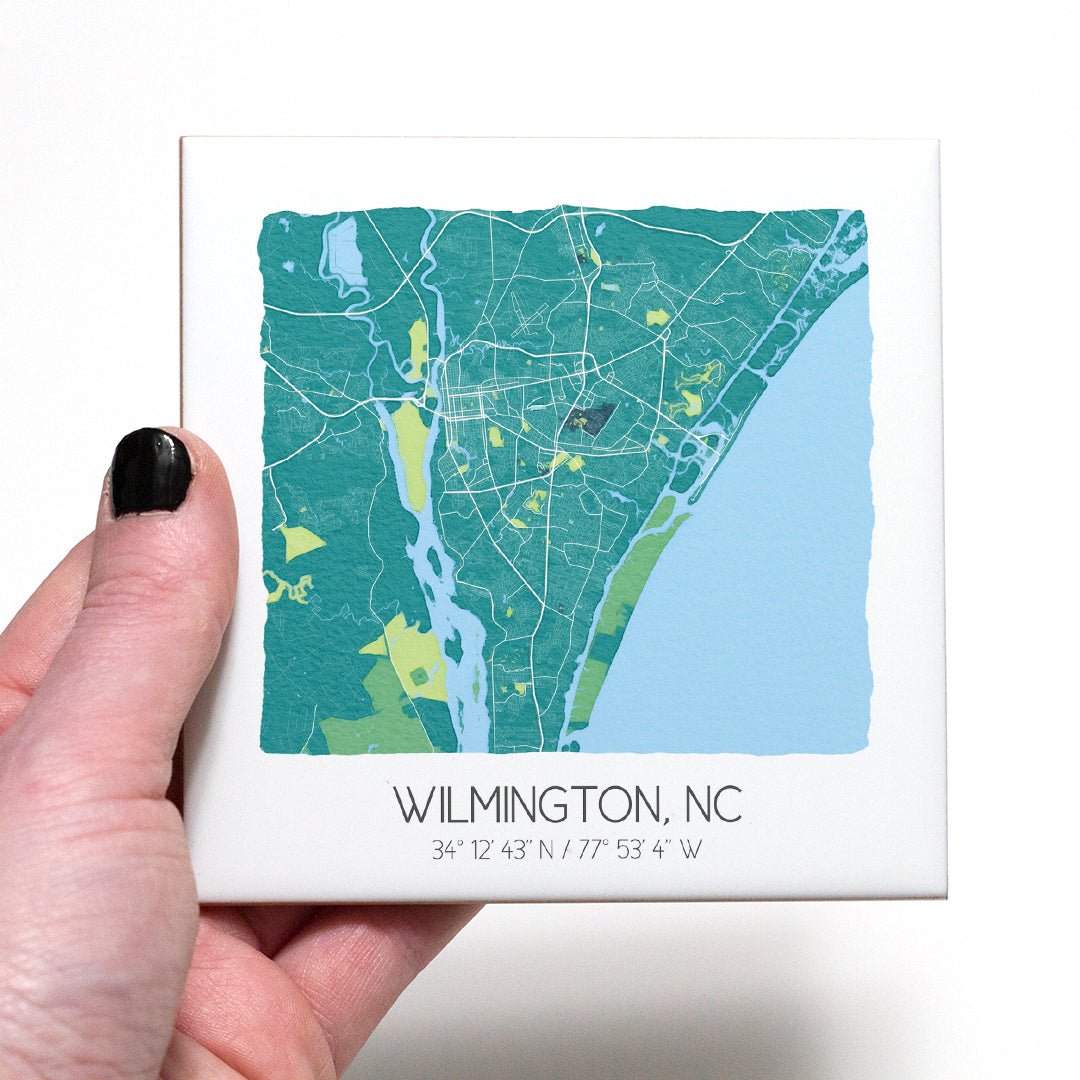 A hand holding a ceramic map coaster of Wilmington NC - in the color teal