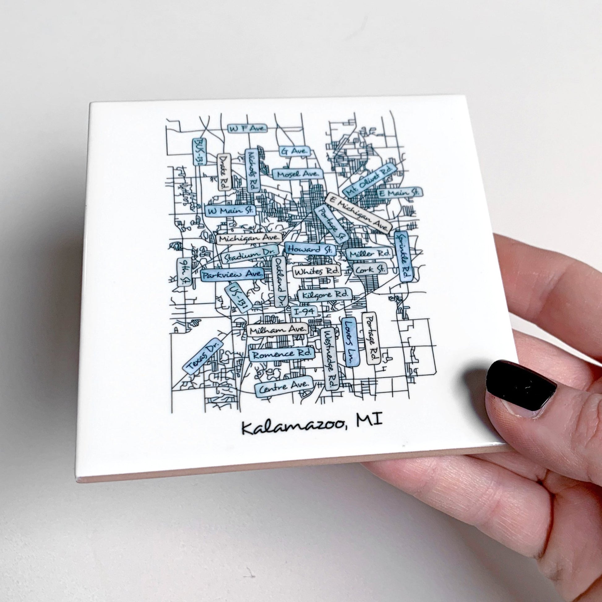 A hand holding a ceramic coaster with a hand-drawn street map on it, showing the tile edges